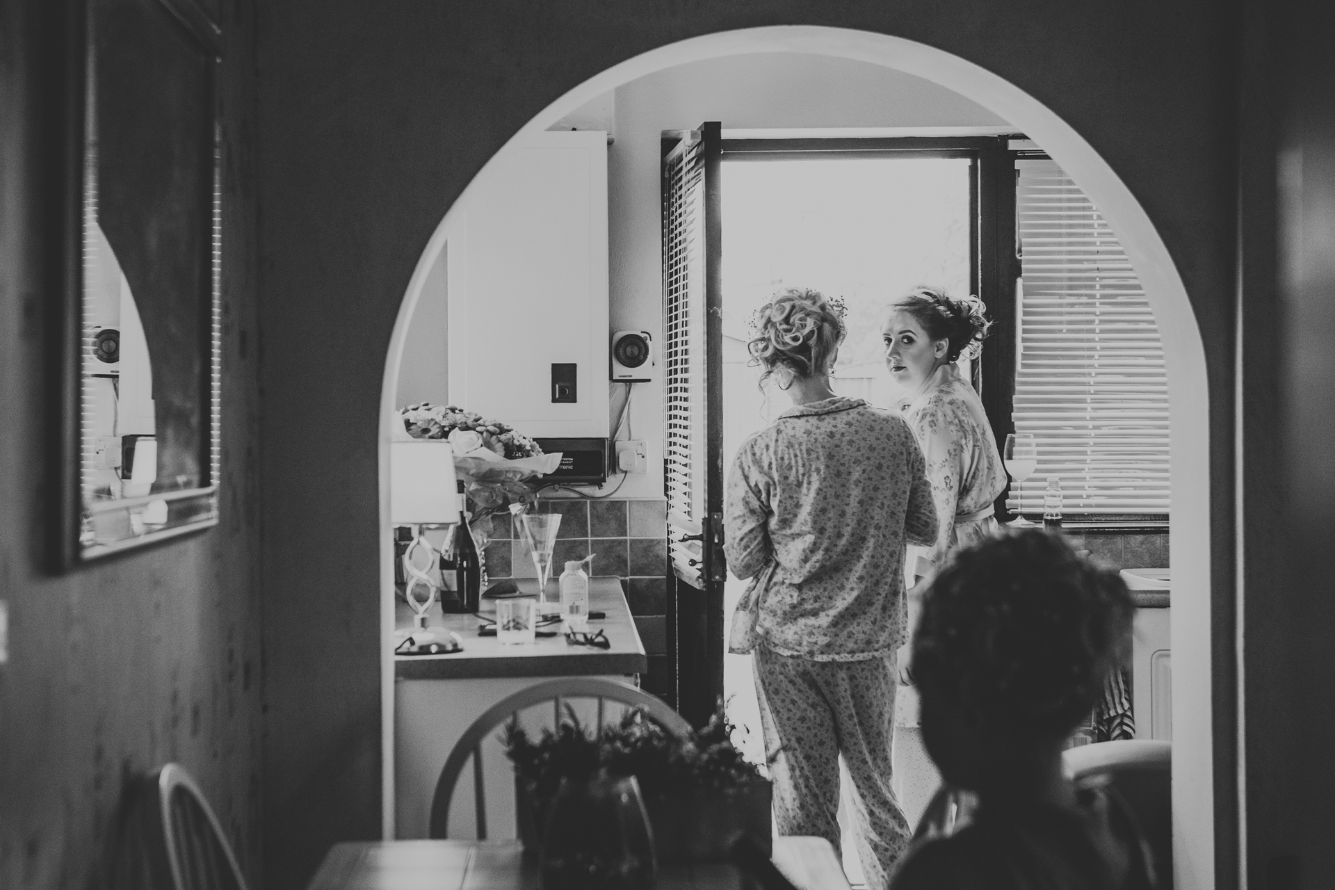 Bride stands in doorway framed by an arch. Photo in black and white. 