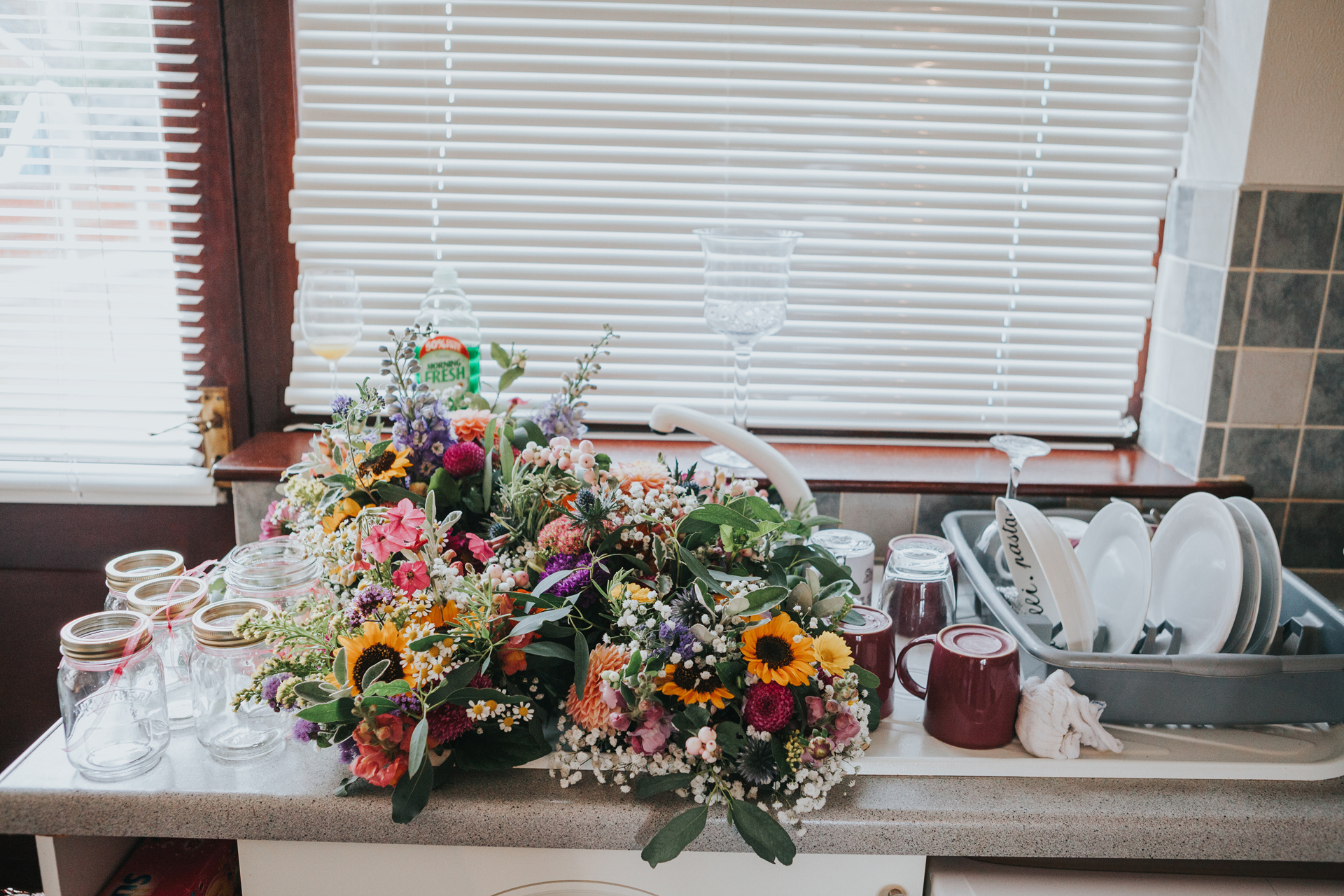 Flowers standing in the sink next to the drying dishes.