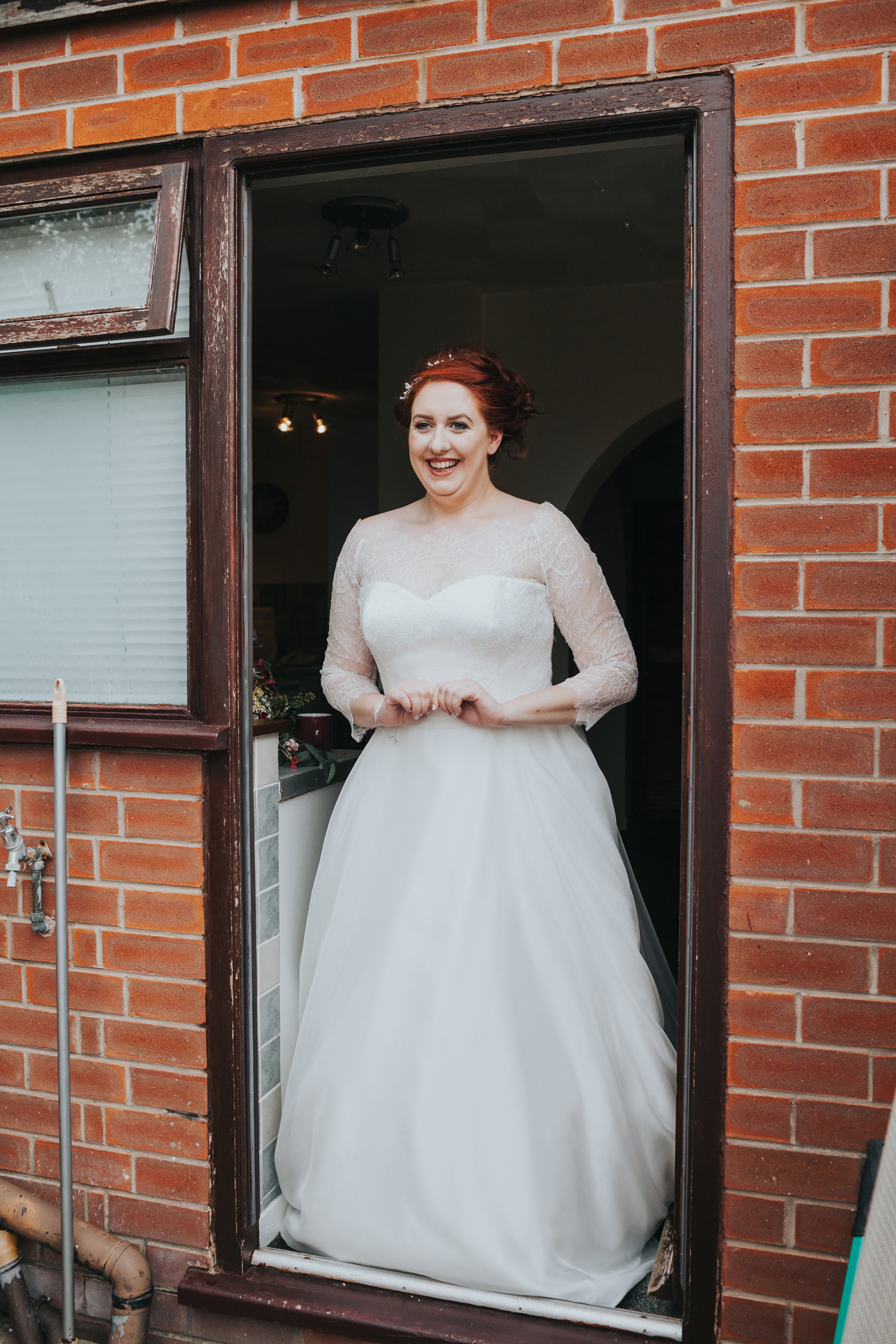 Bride standing at back door in her dress. 