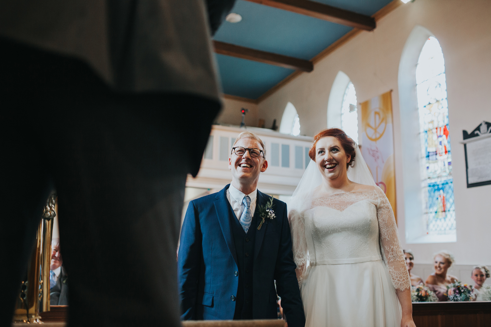 Bride and groom look on smiling as their friend reads. 