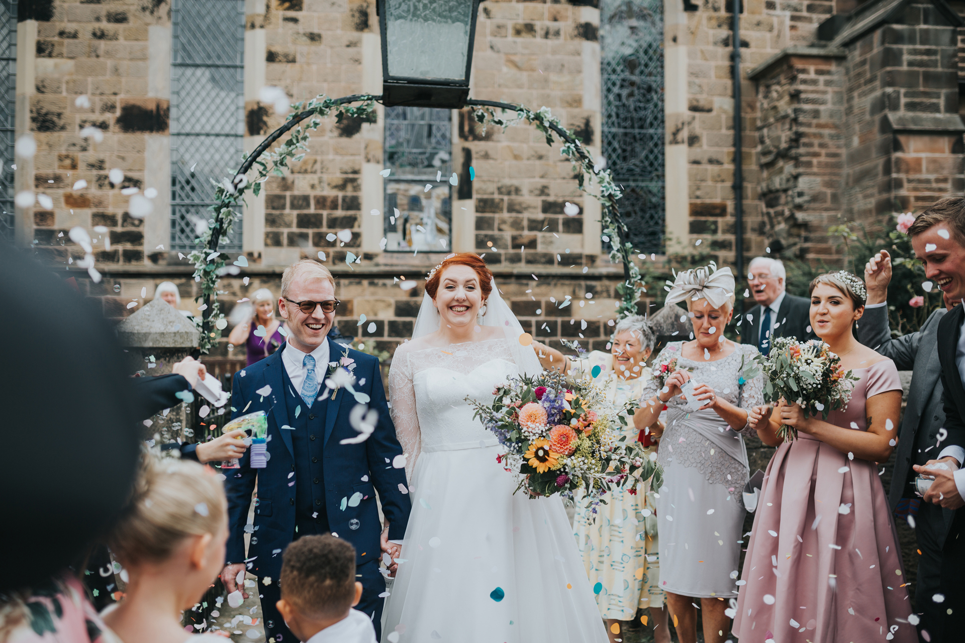 Guests surround bride and groom as they throw confetti at them at St Thomas Church Liverpool