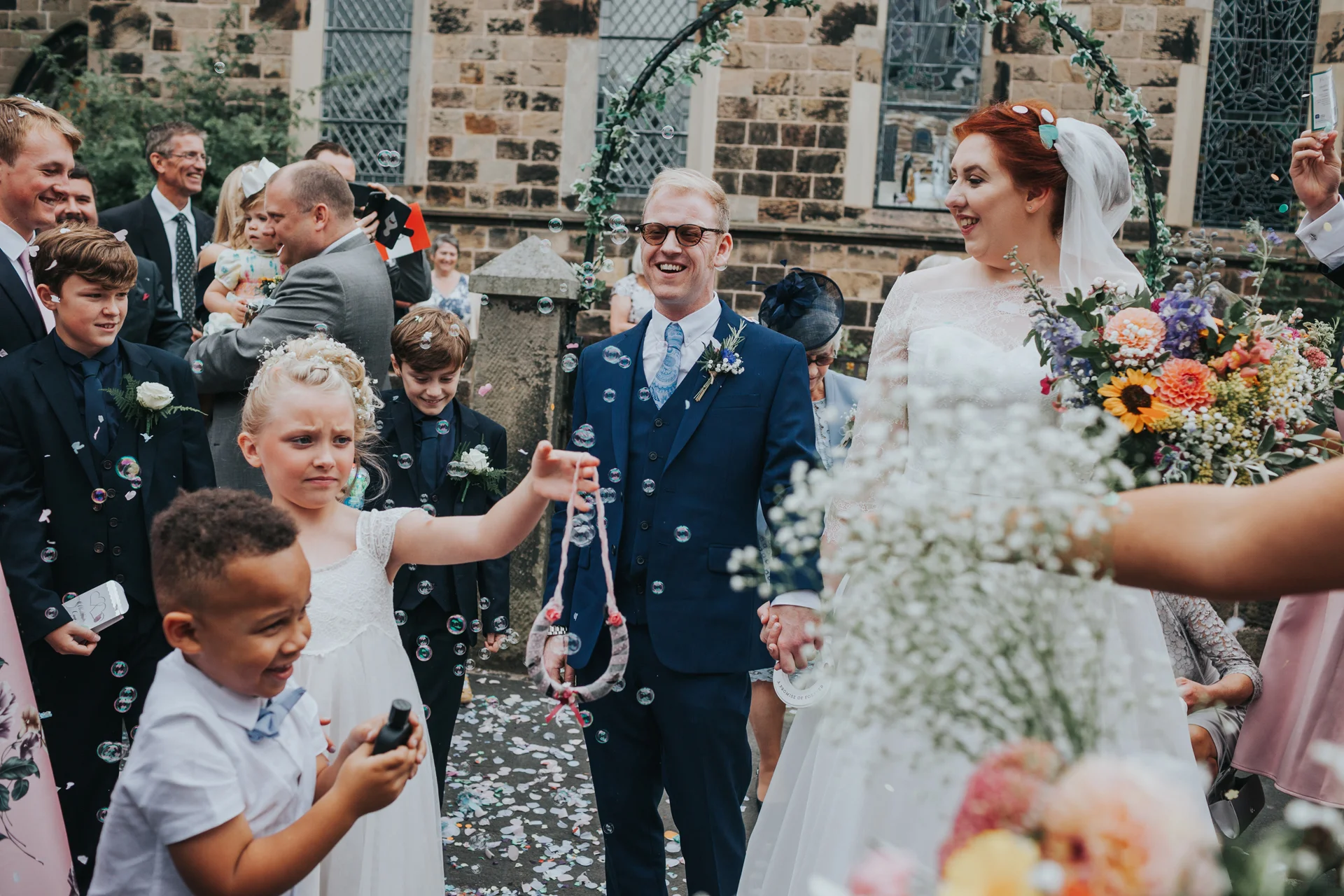 Confetti and bubbles surround bride and groom as they laugh.