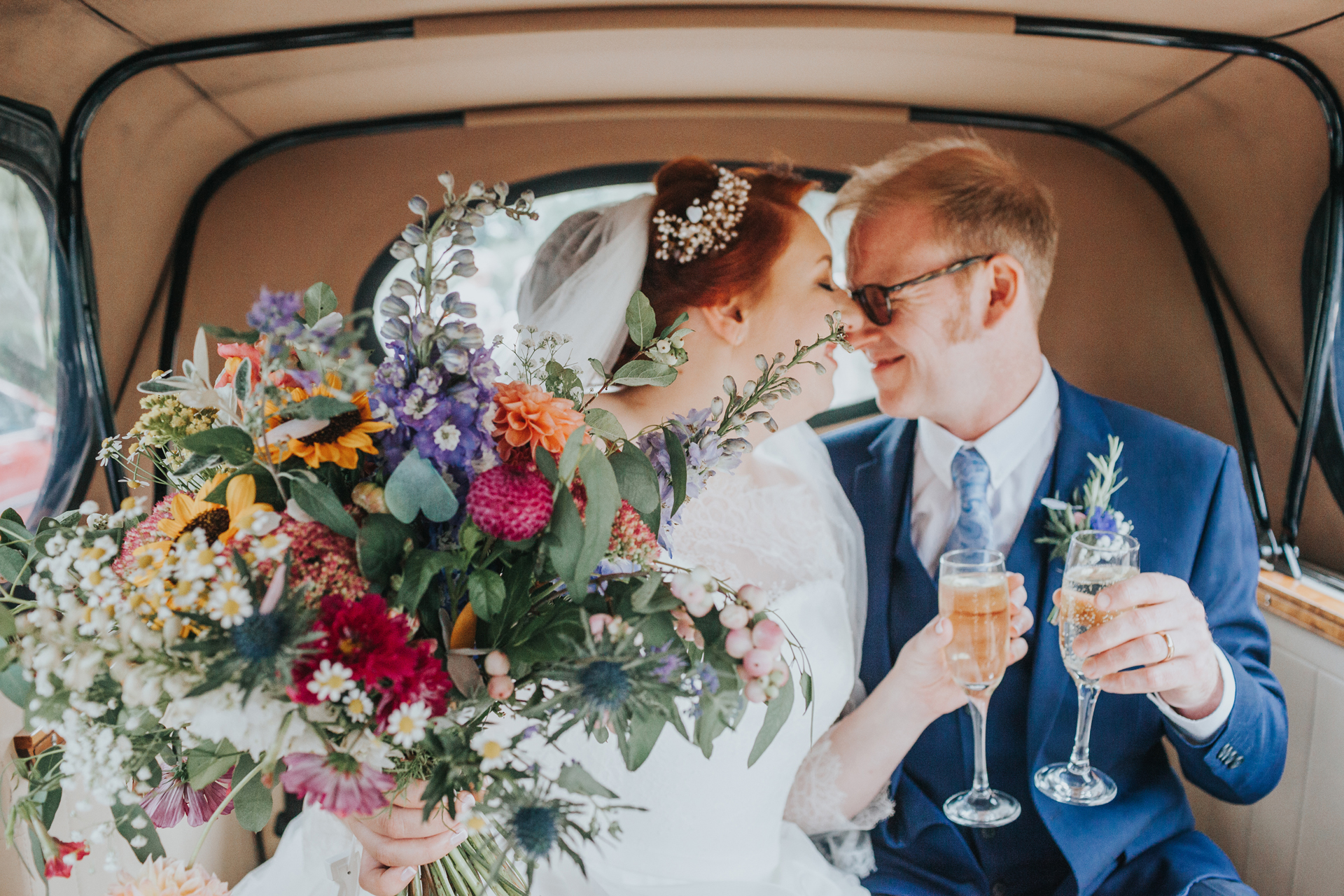Bride and groom have a kiss in the back on the wedding car, focus on the brides bouquet.