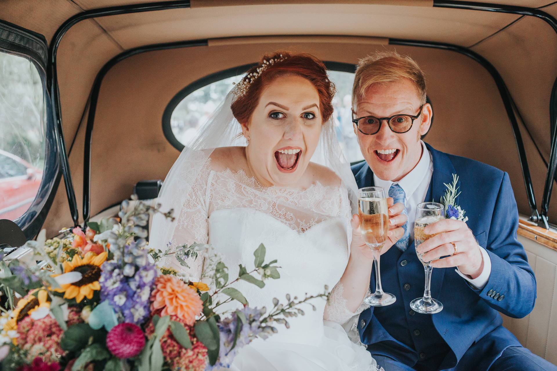 Bride and groom have excited faces in the back on the wedding car.