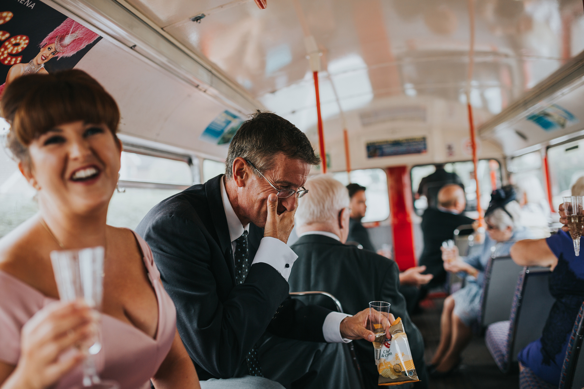 Guests laugh on the top deck of the wedding bus. 