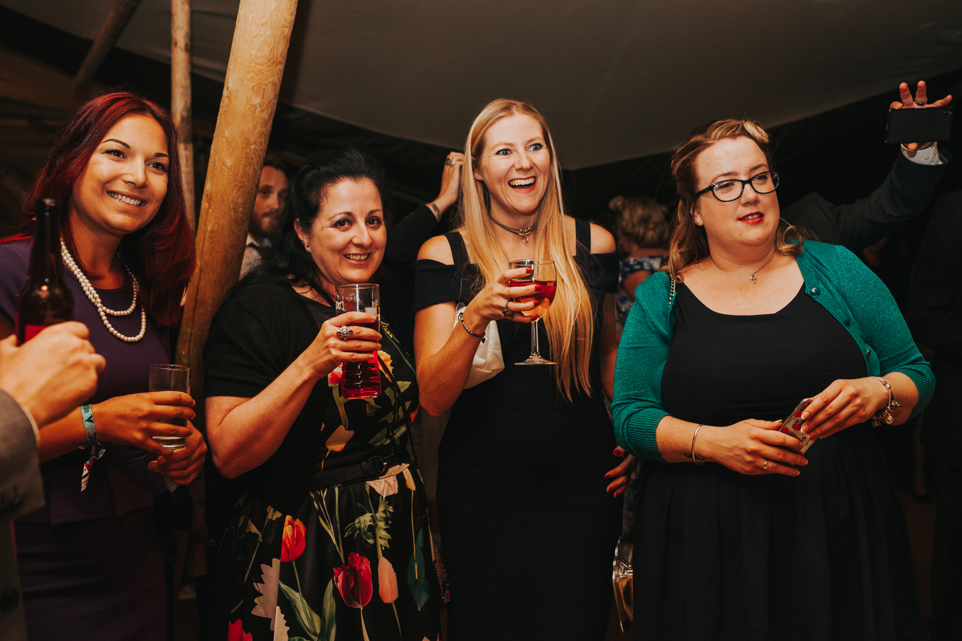 Guests watching the cake being cut while holding drinks.