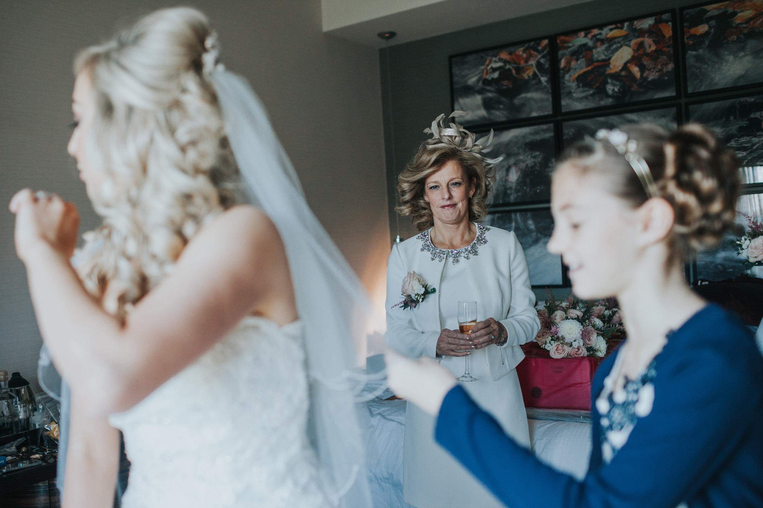 Mother of the Bride looks proudly as her daughter puts on her wedding dress. 