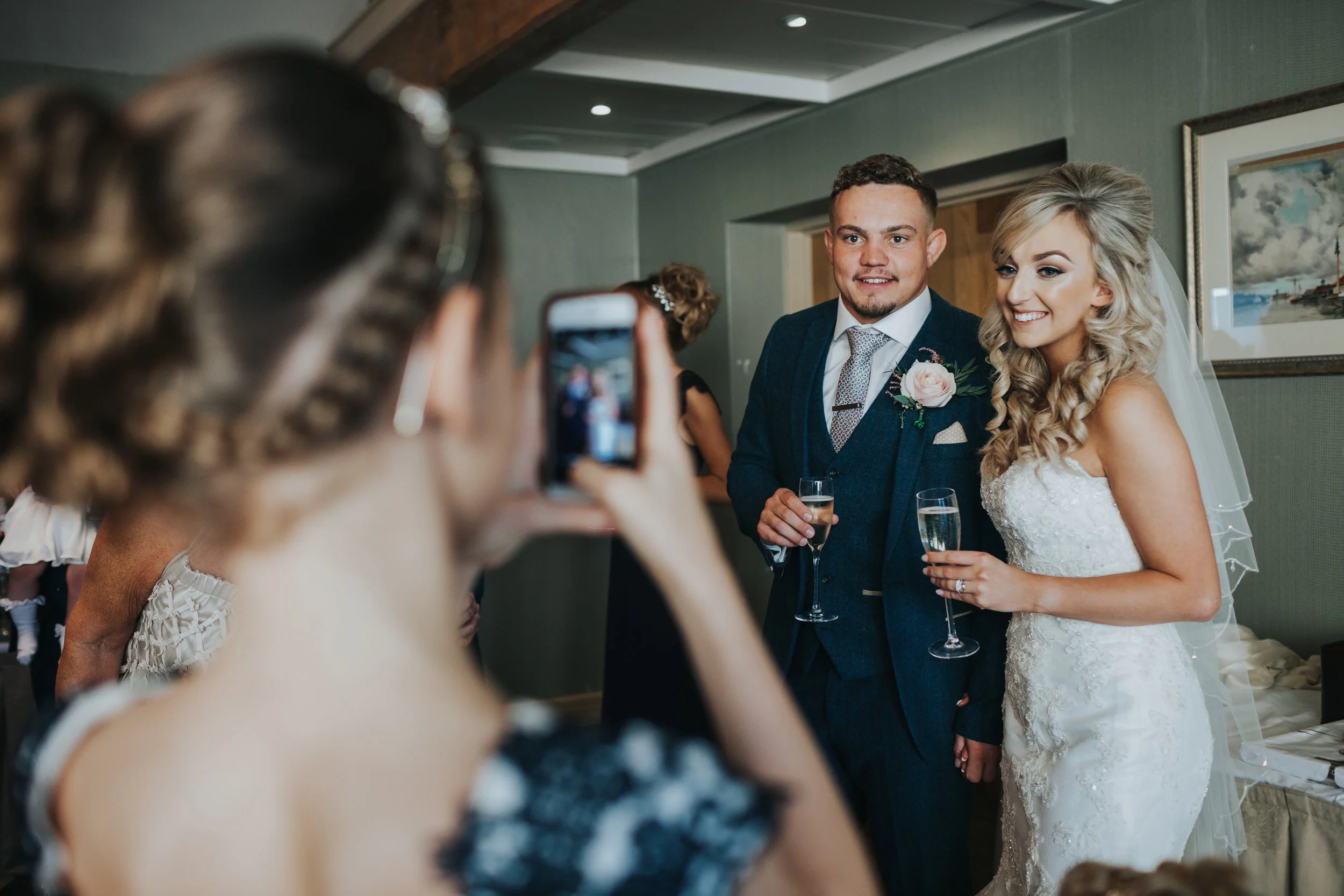 Bride and groom pose for their flower girl to take a photograph on her phone. 