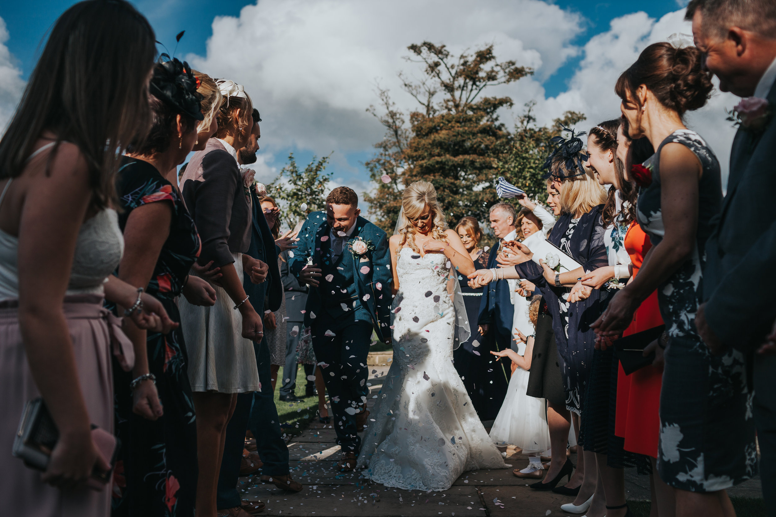 Bride and groom walk between guests as wedding guests throw confetti at them. 