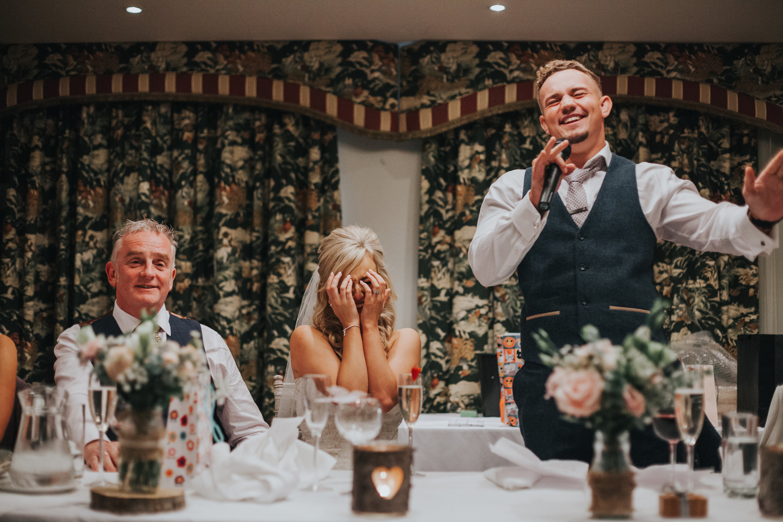 Bride holds hands over her face as her husband makes his speech. 