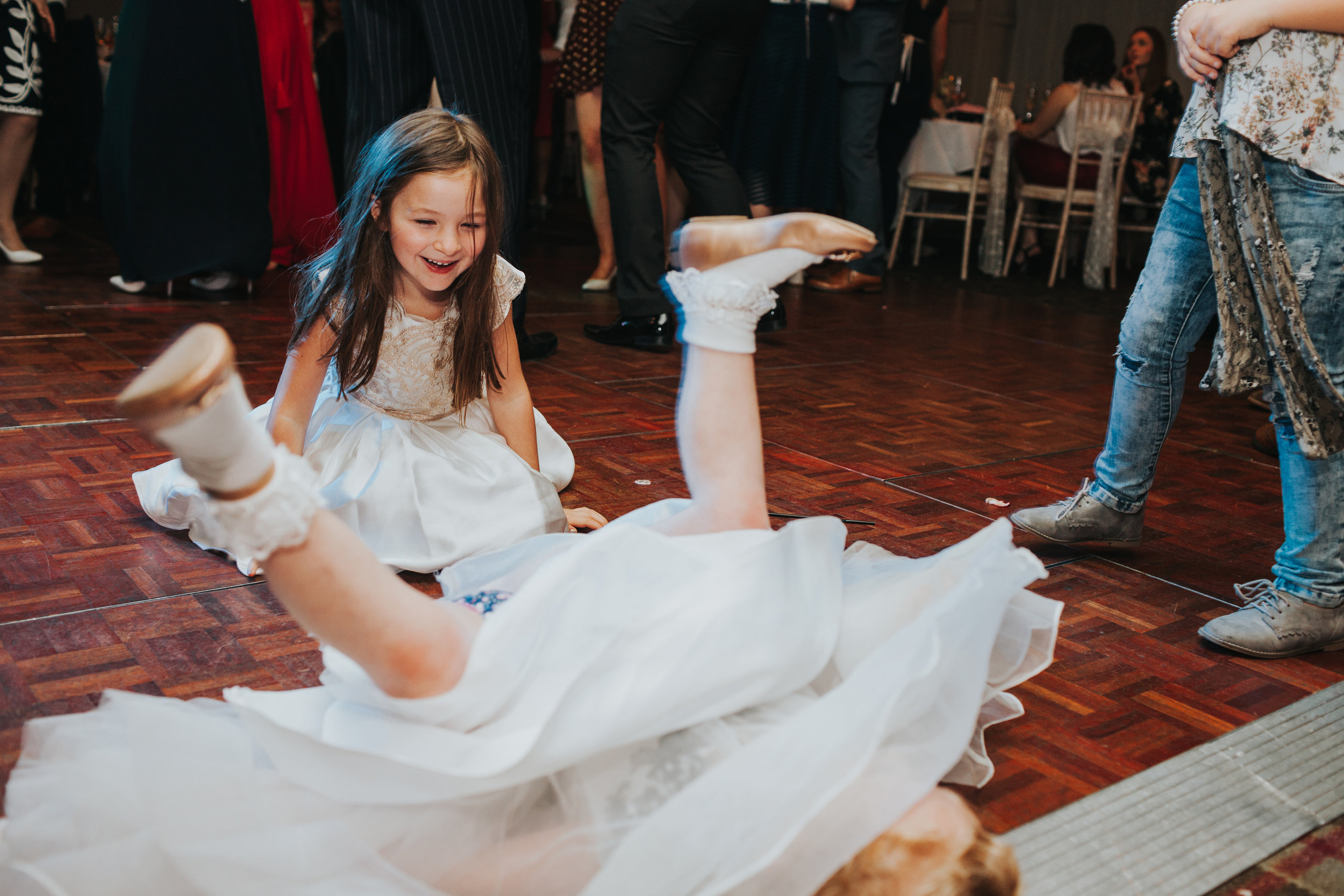 Little girl laughs at her friend who has fallen backwards on the floor.