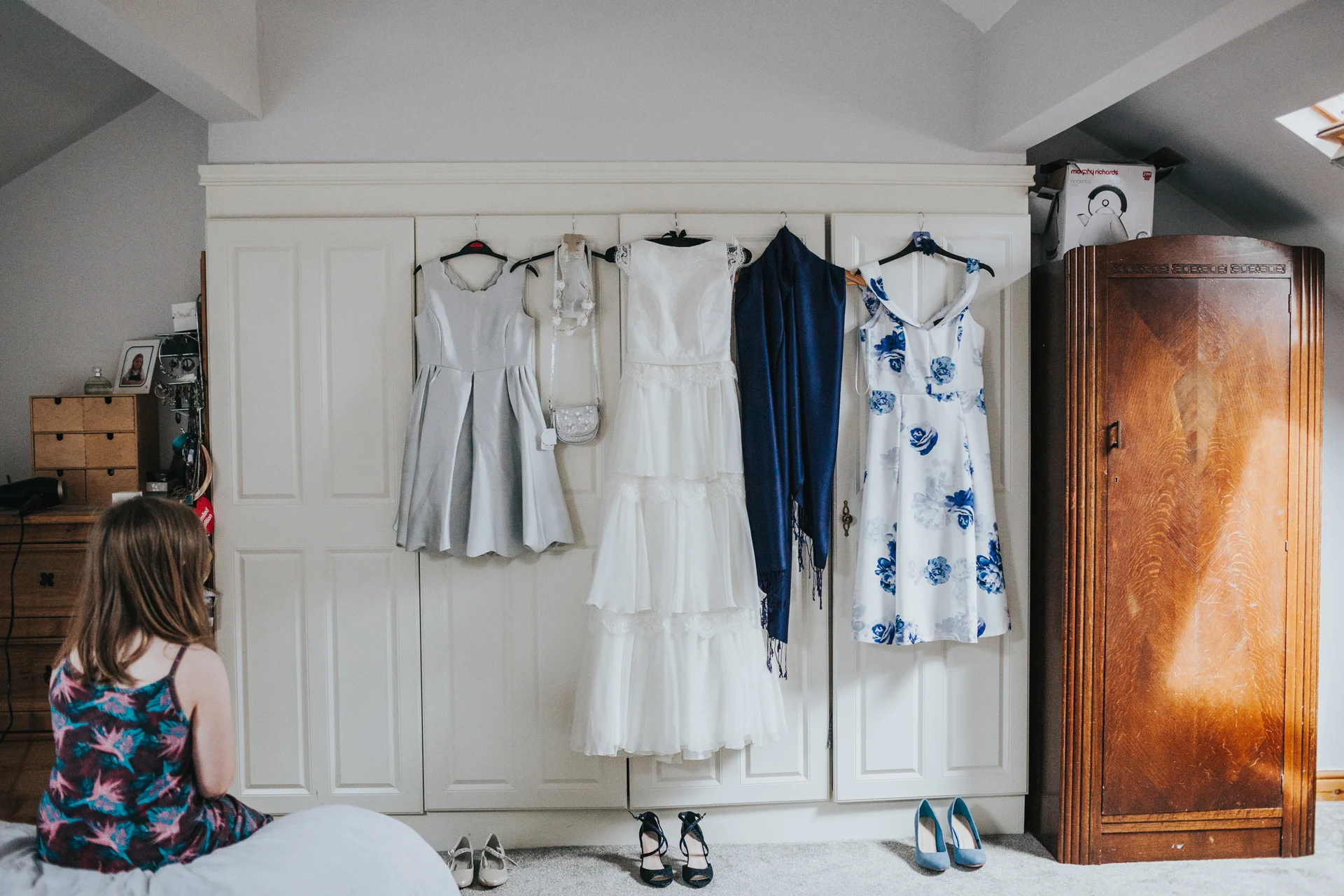 Little girl looks on at Brides Dress hanging up. 