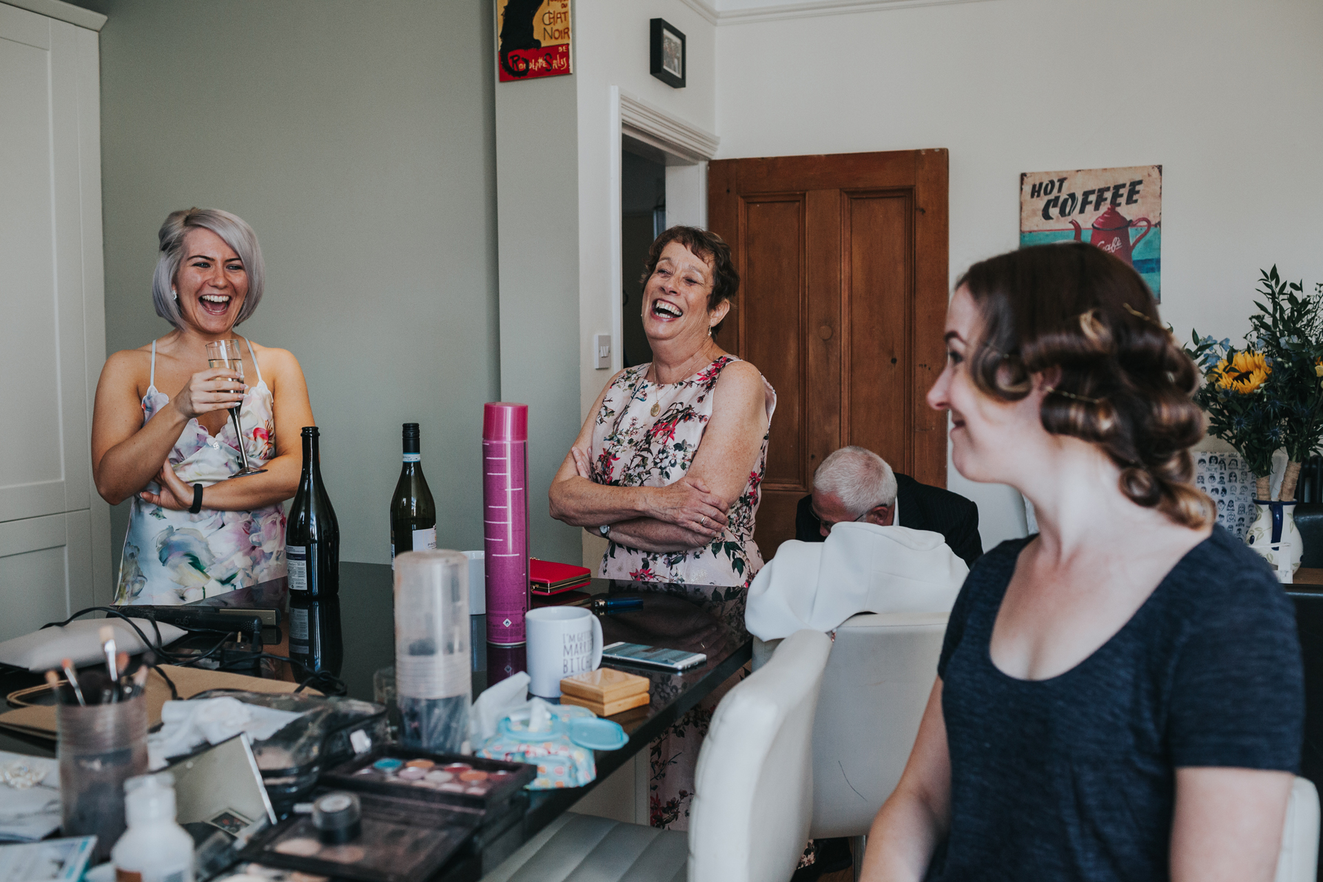 Bridal party laugh together in brides kitchen as she gets ready for her wedding. 