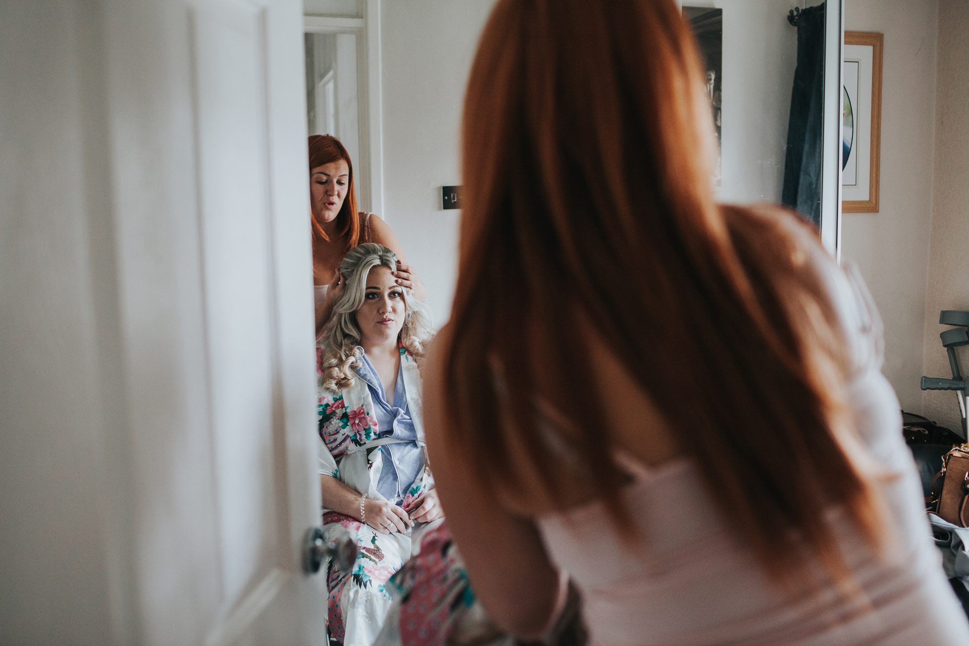 Camera peeking through the doorway to catch brides reflection in the mirror as she has her hair done. 