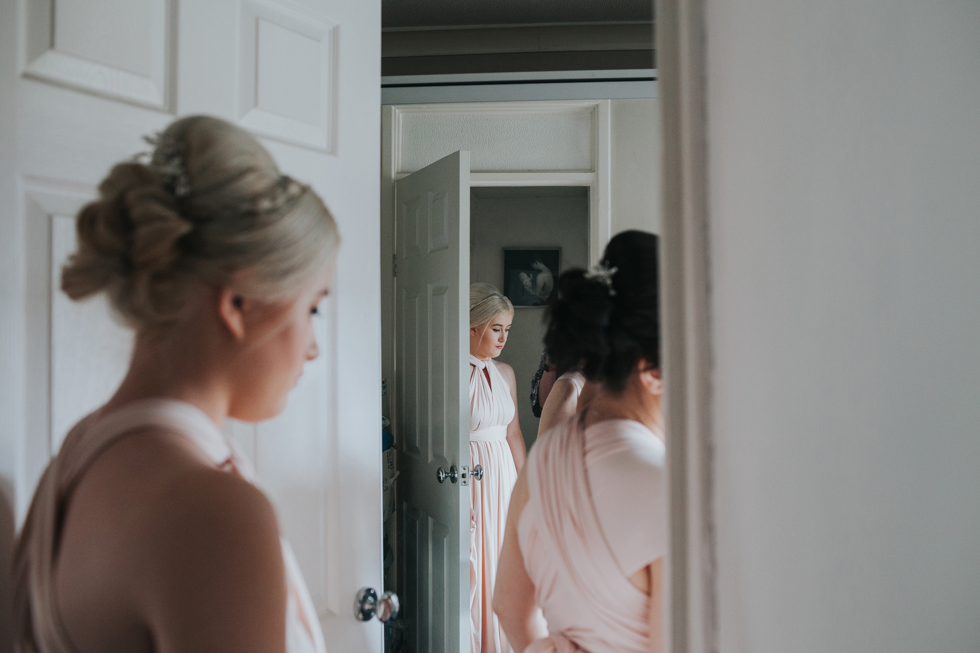Bridesmaid waits outside the door for the bride, we see her in the foreground and back ground of the photograph as she is reflected in the mirror beyond the door. 