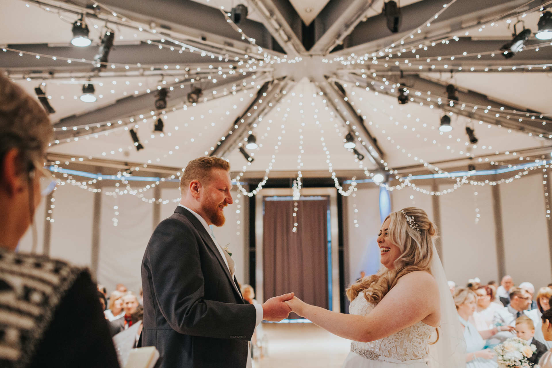 Bride and Groom hold hands with fairy lights twinkling behind them. 