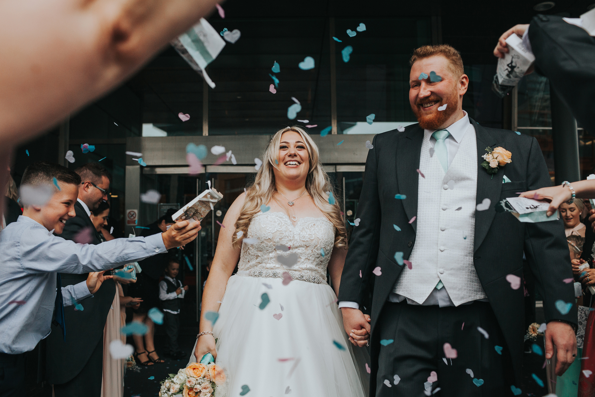 Bride and Groom look happy as they have confetti thrown at them from all angles. 