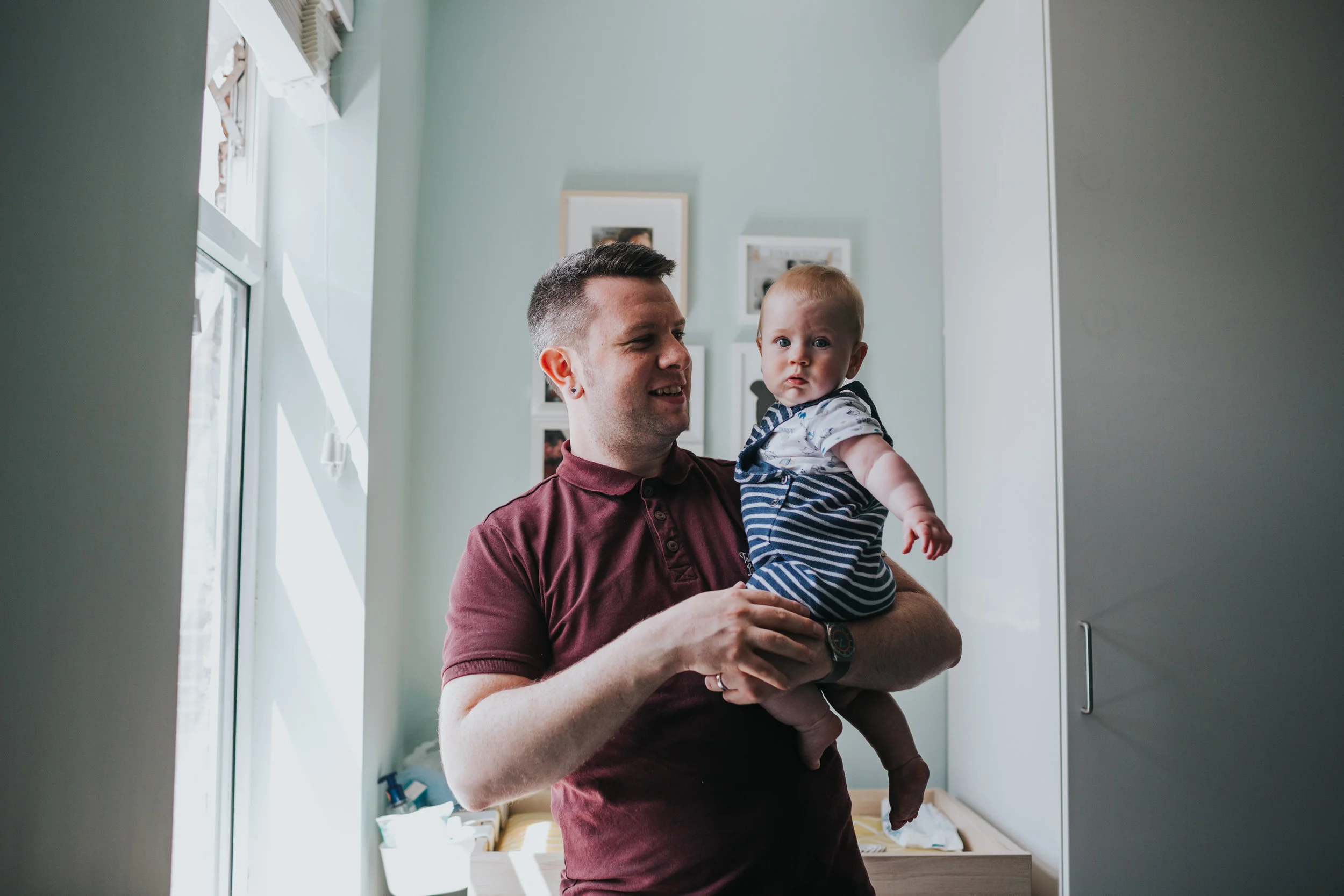 Dad and baby standing in the window light.