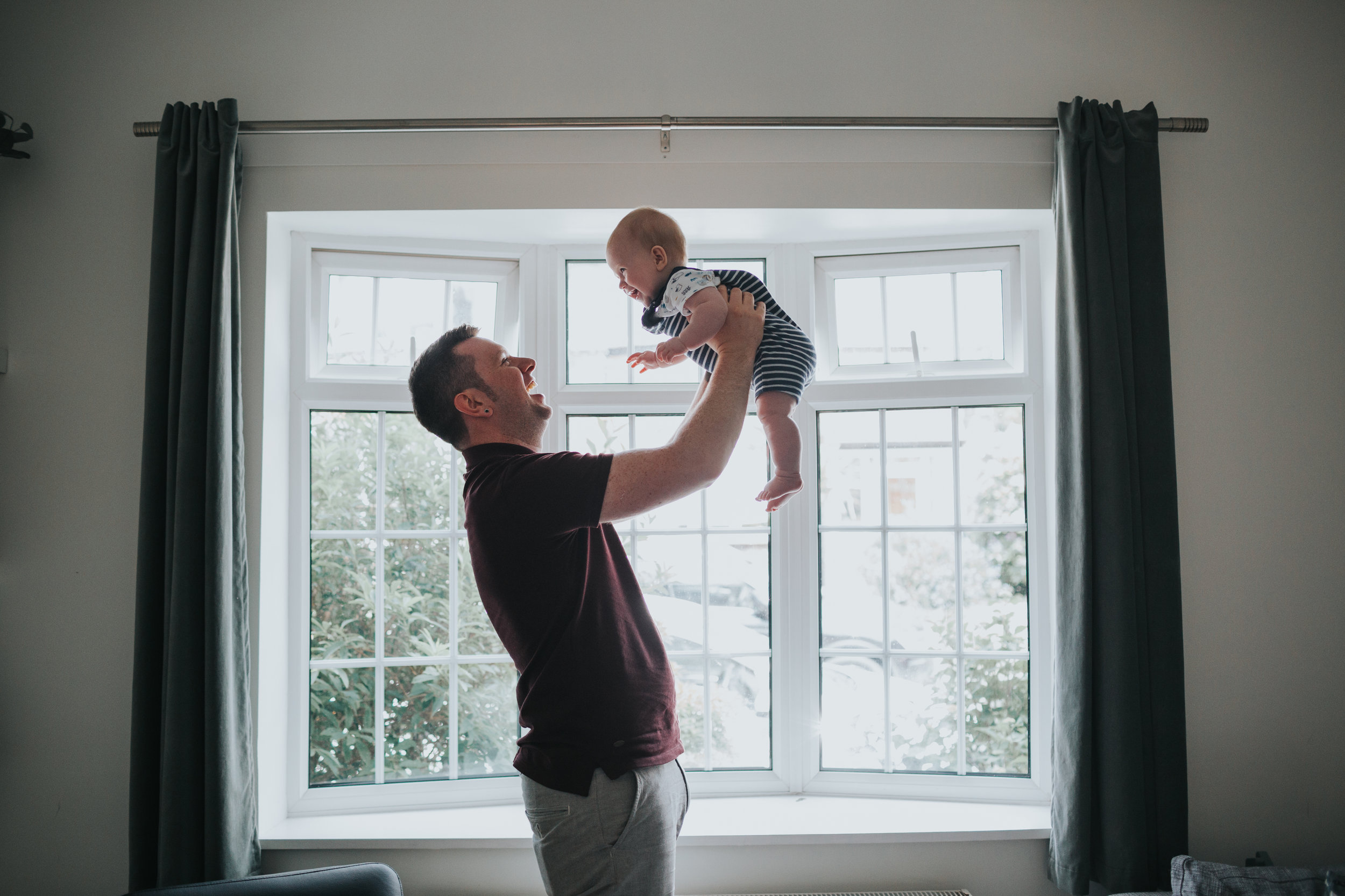 Dad chucks baby up and down in font of window to celebrate. 