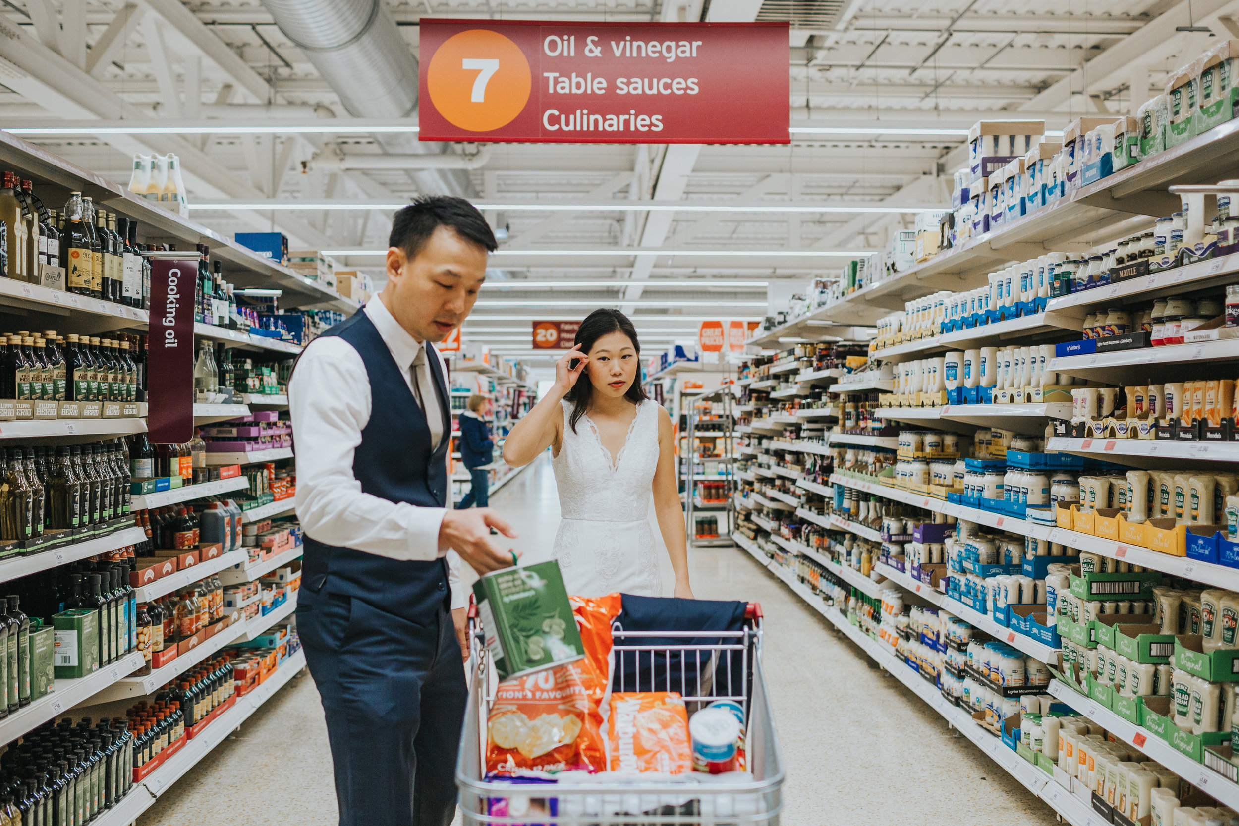 Couple in supermarket shopping wearing full wedding outfits. 