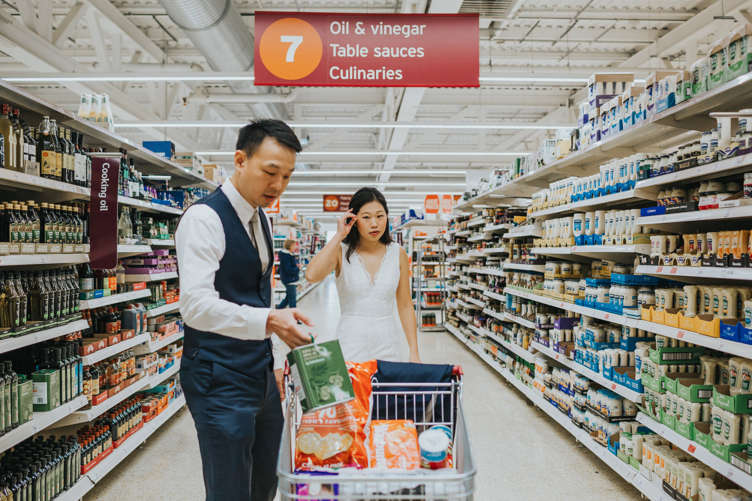 Couple in supermarket shopping wearing full wedding outfits.