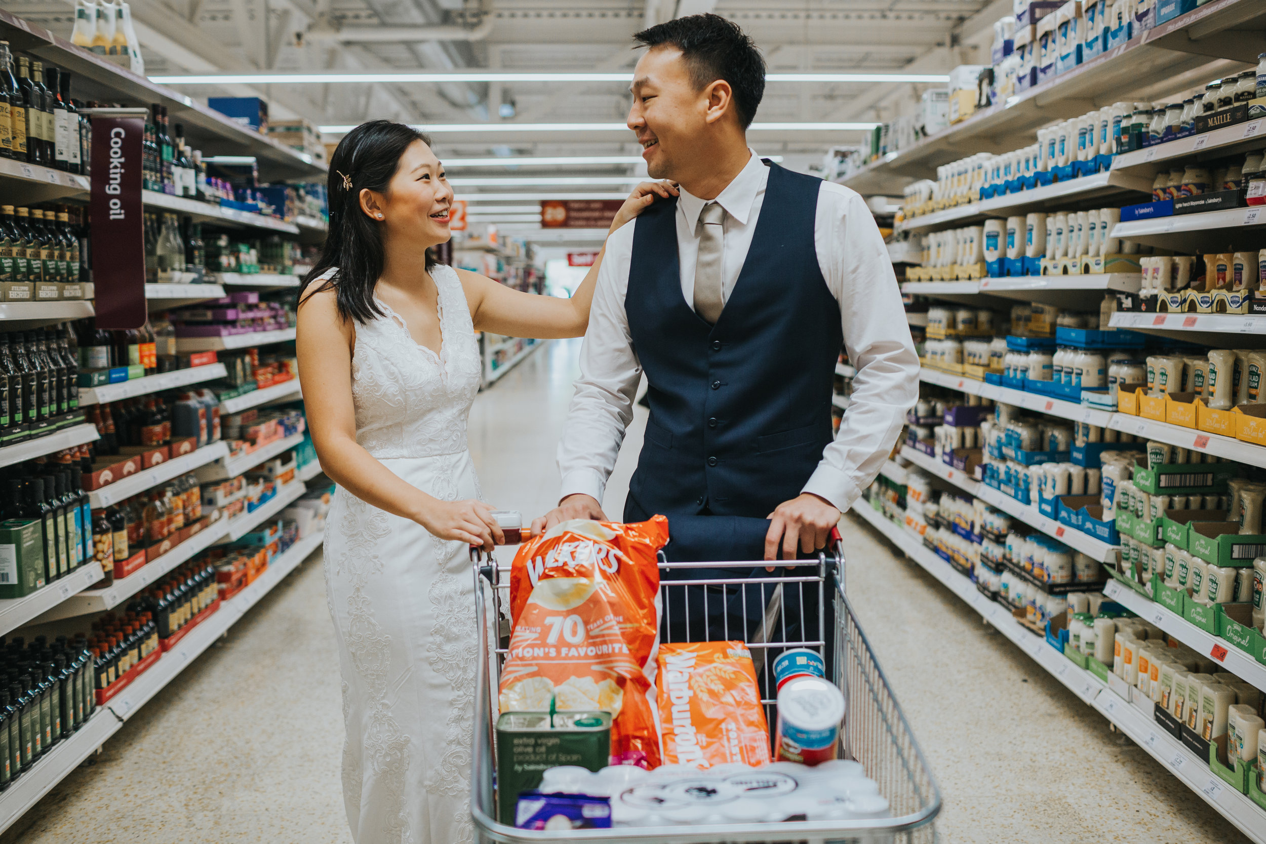 Couple pause together with shopping trolly in supermarket, Manchester. 