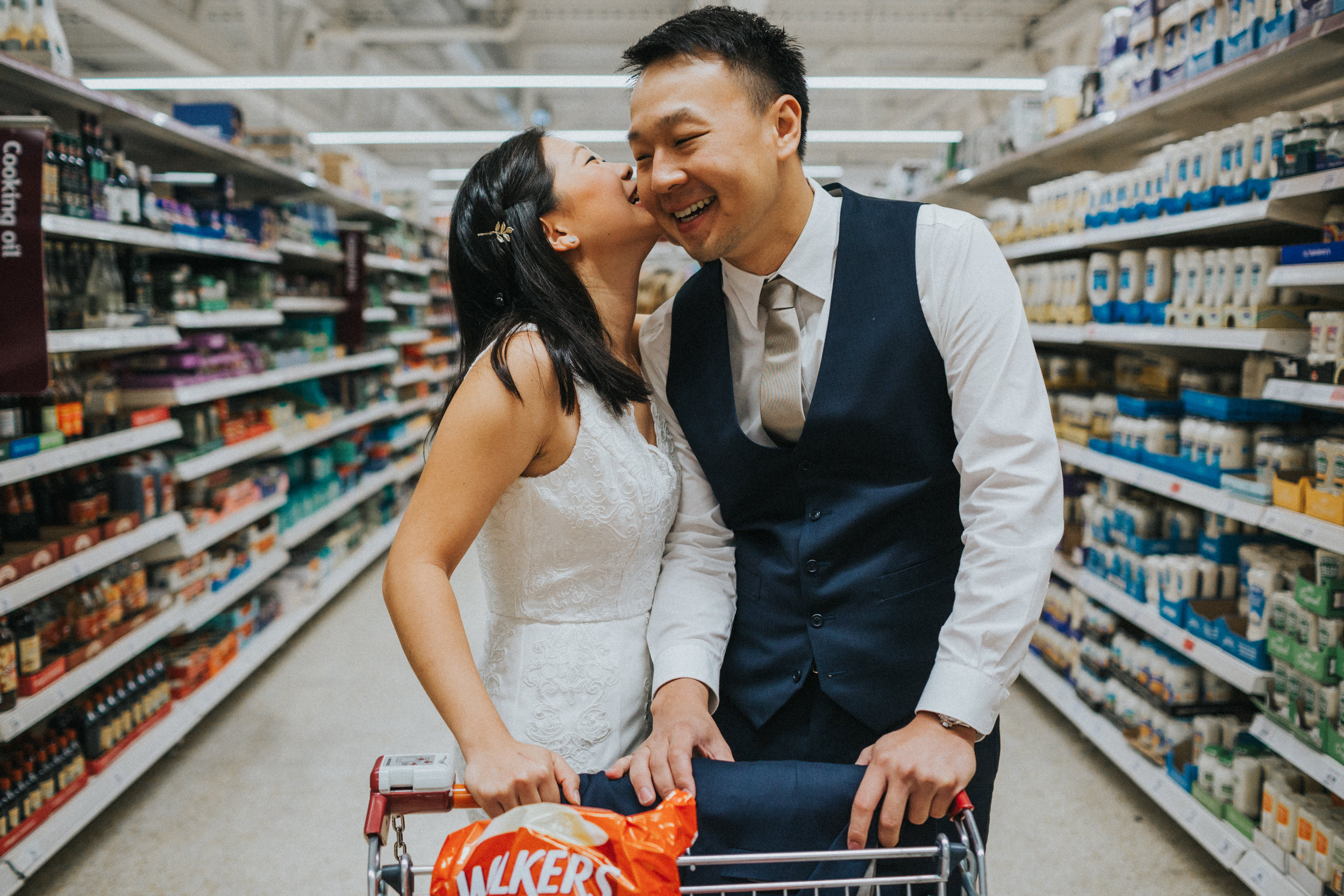 Bride whispers into grooms ear in supermarket. 