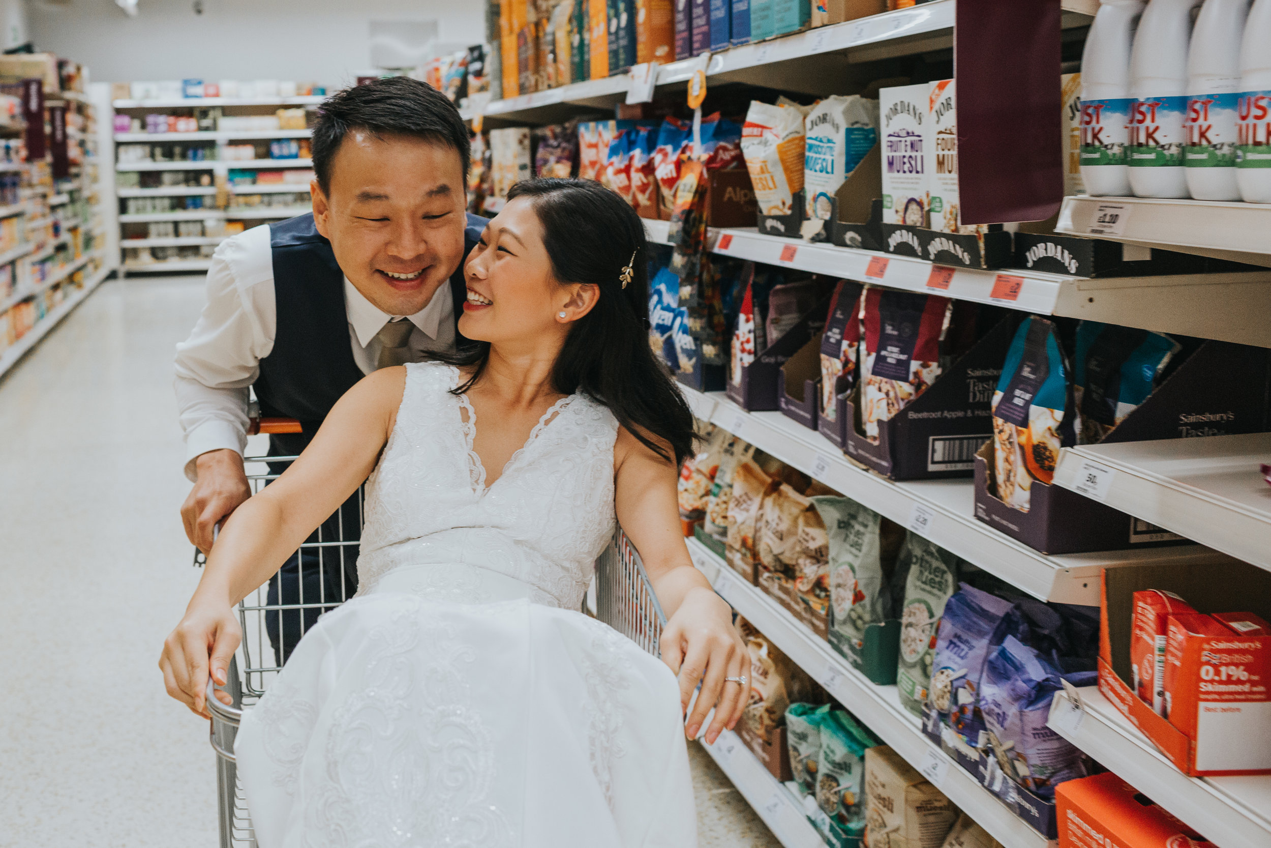 Couple have a moment together as bride sits back in shopping trolley. 