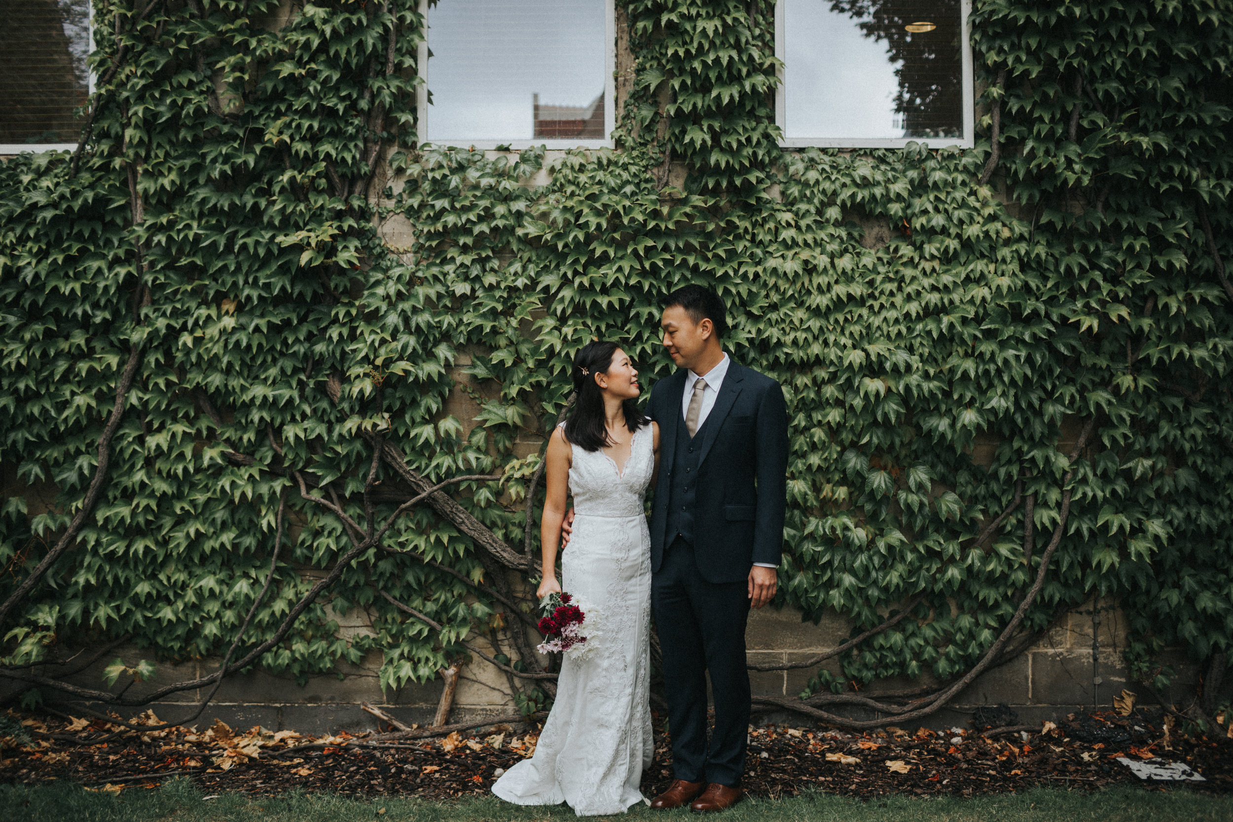 Couple stand together in front of a wall full of Ivy at Manchester University. 