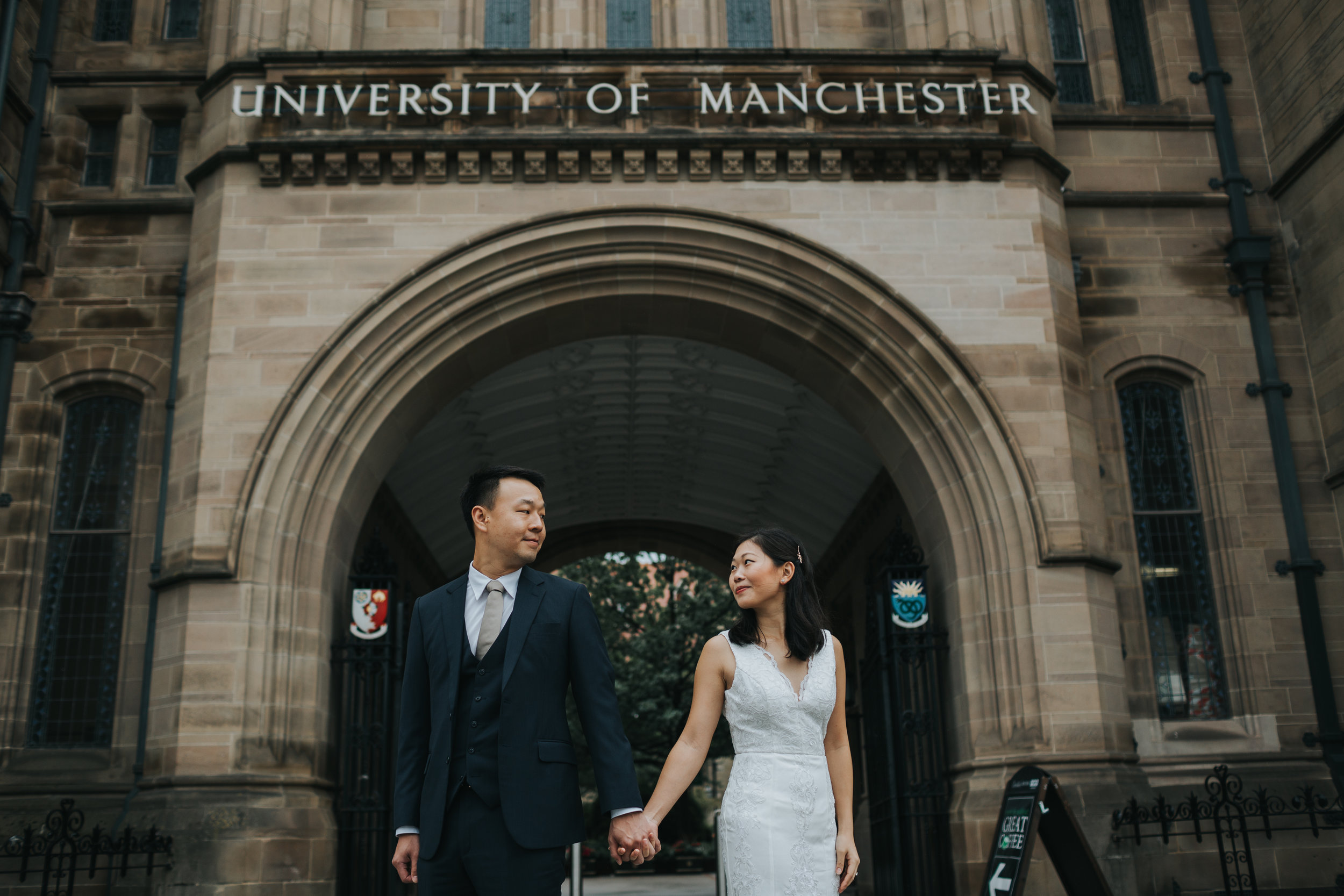 Couple stand together under Manchester University sign. 