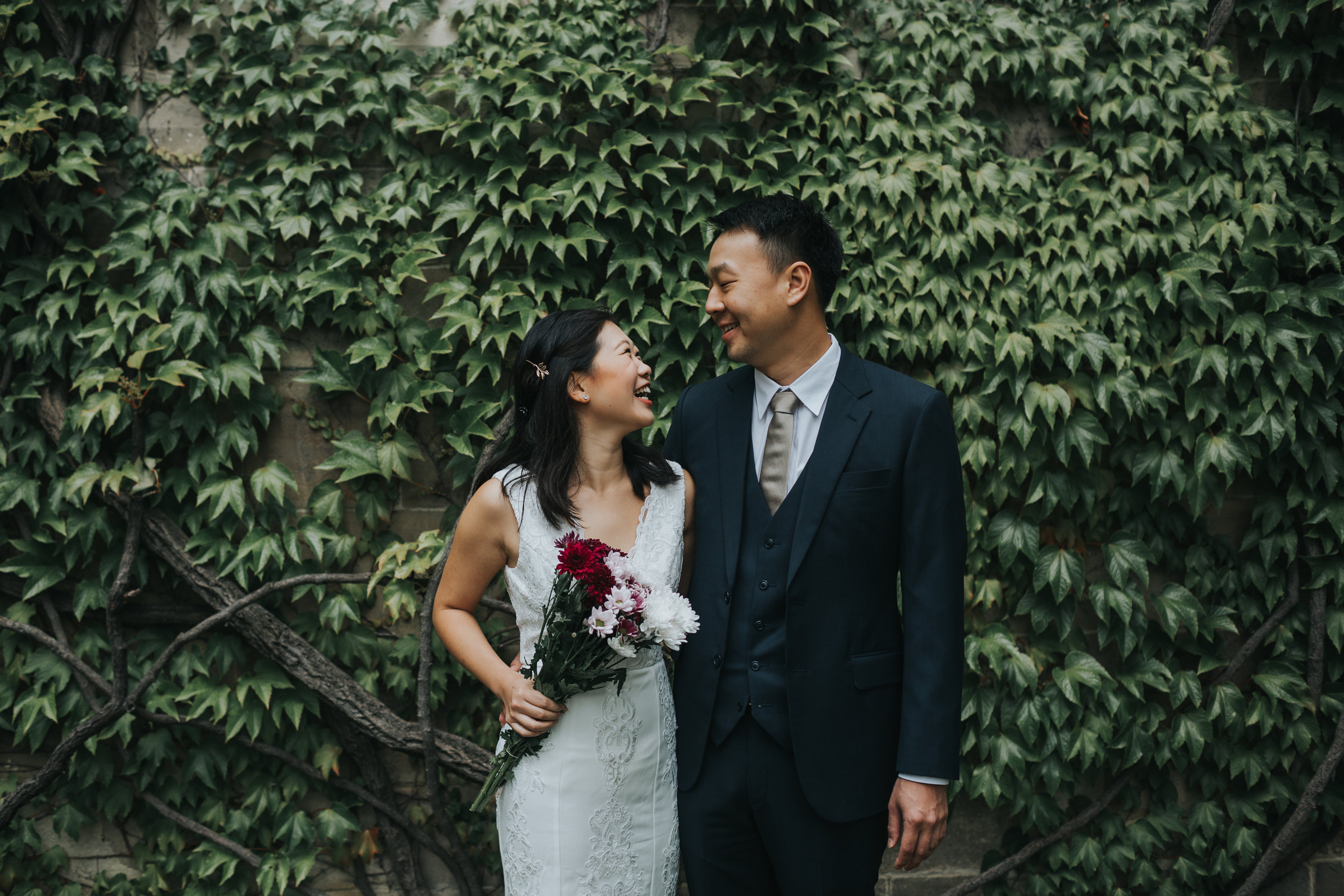 Bride and Groom laughing together in front of a wall full of ivy.  
