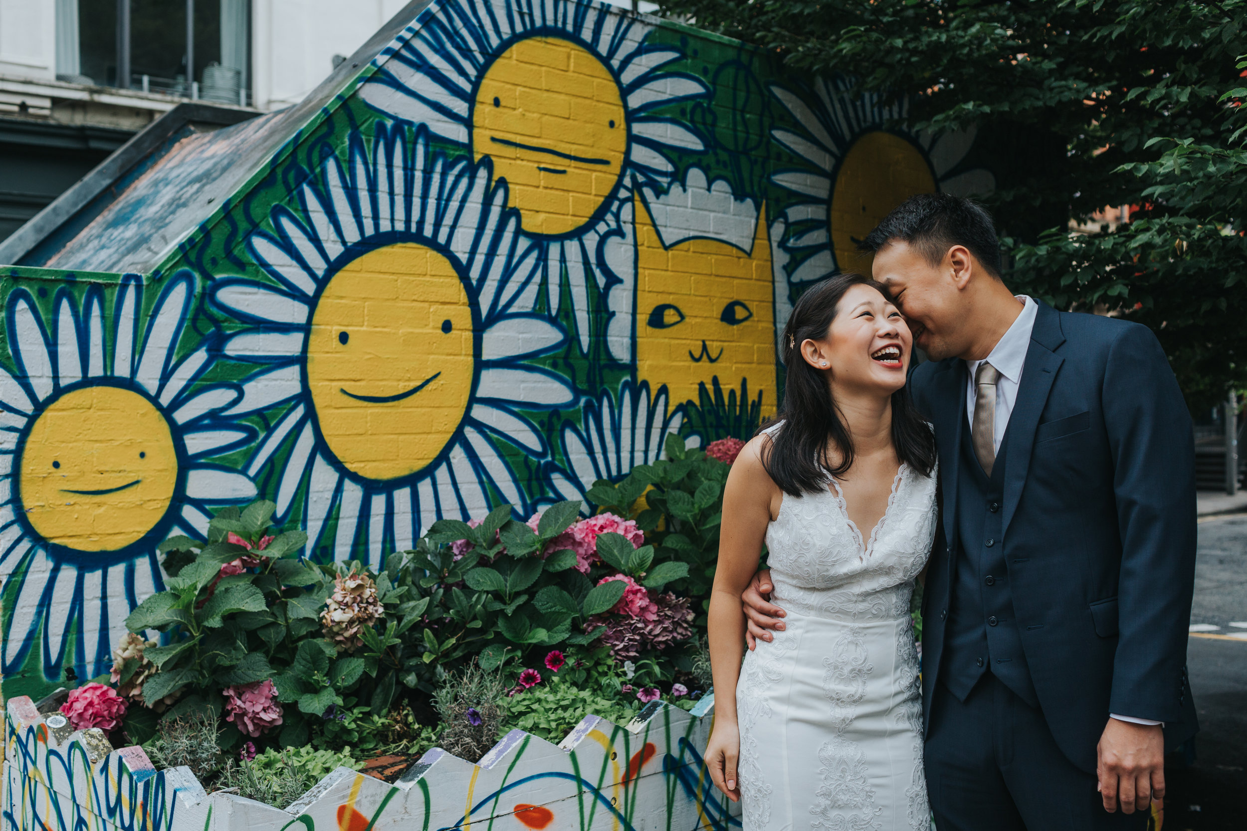 Couple laughing together in front of sunshine graffiti in Manchester's Northern Quarter. 