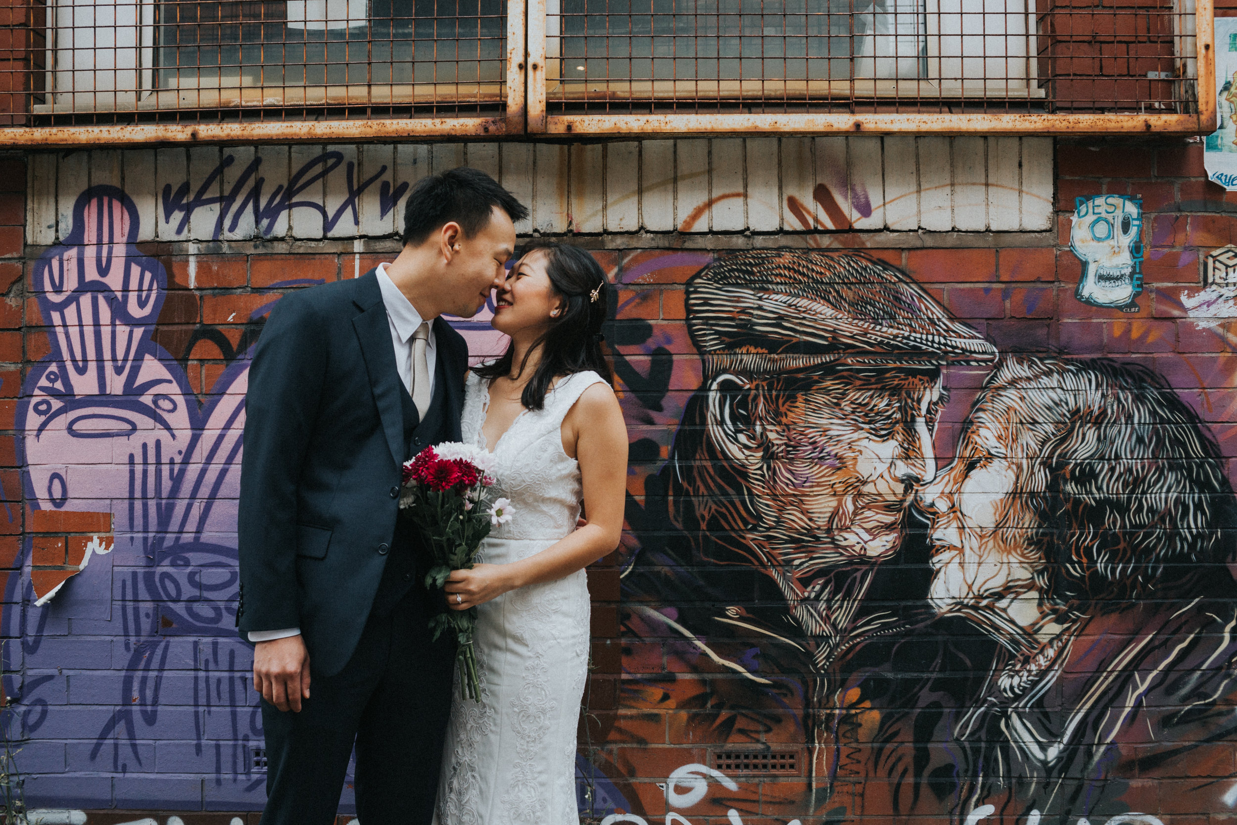 Couple give each other an eskimo kiss in front of old couple graffiti. 