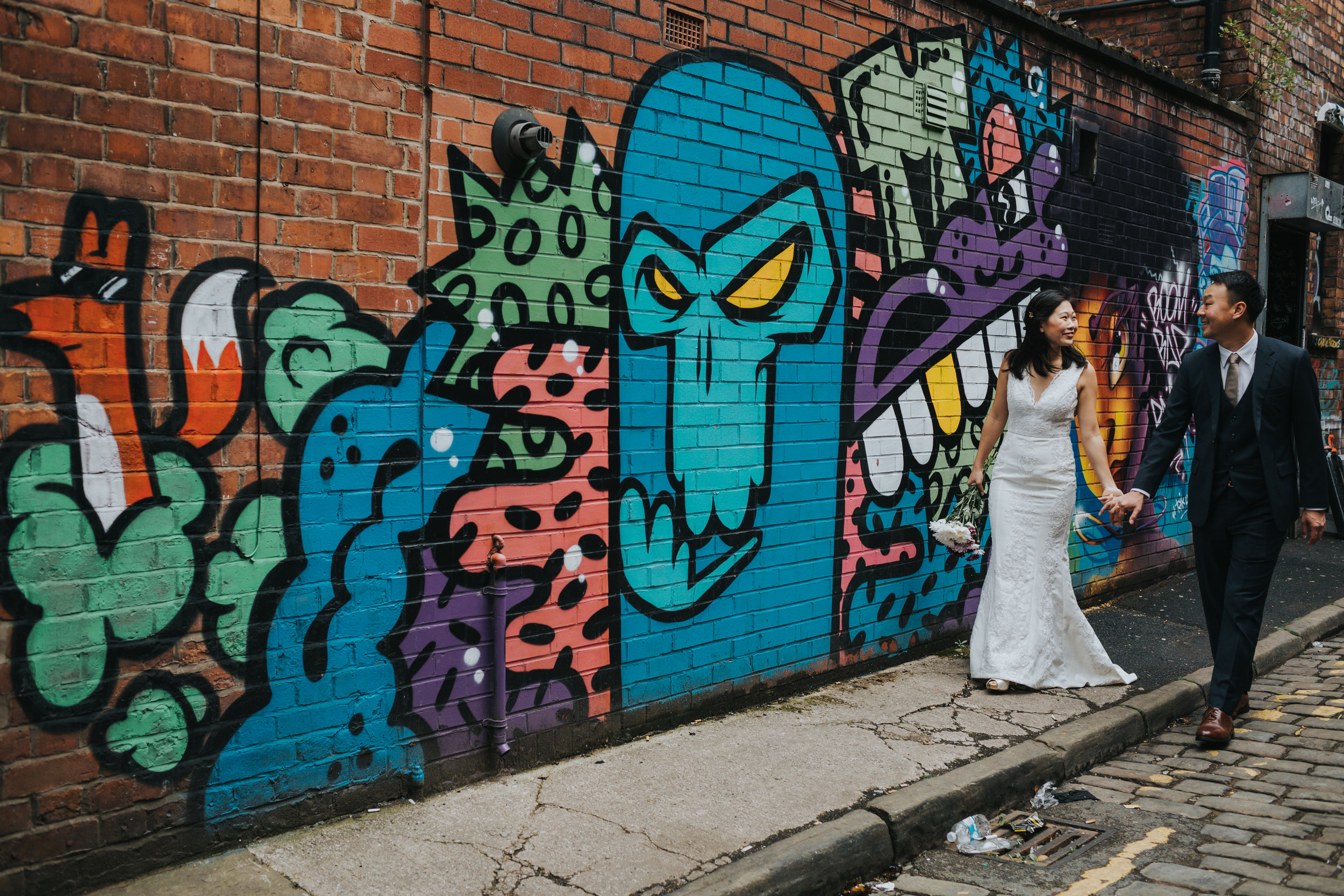 Couple walk along colourful graffiti. 