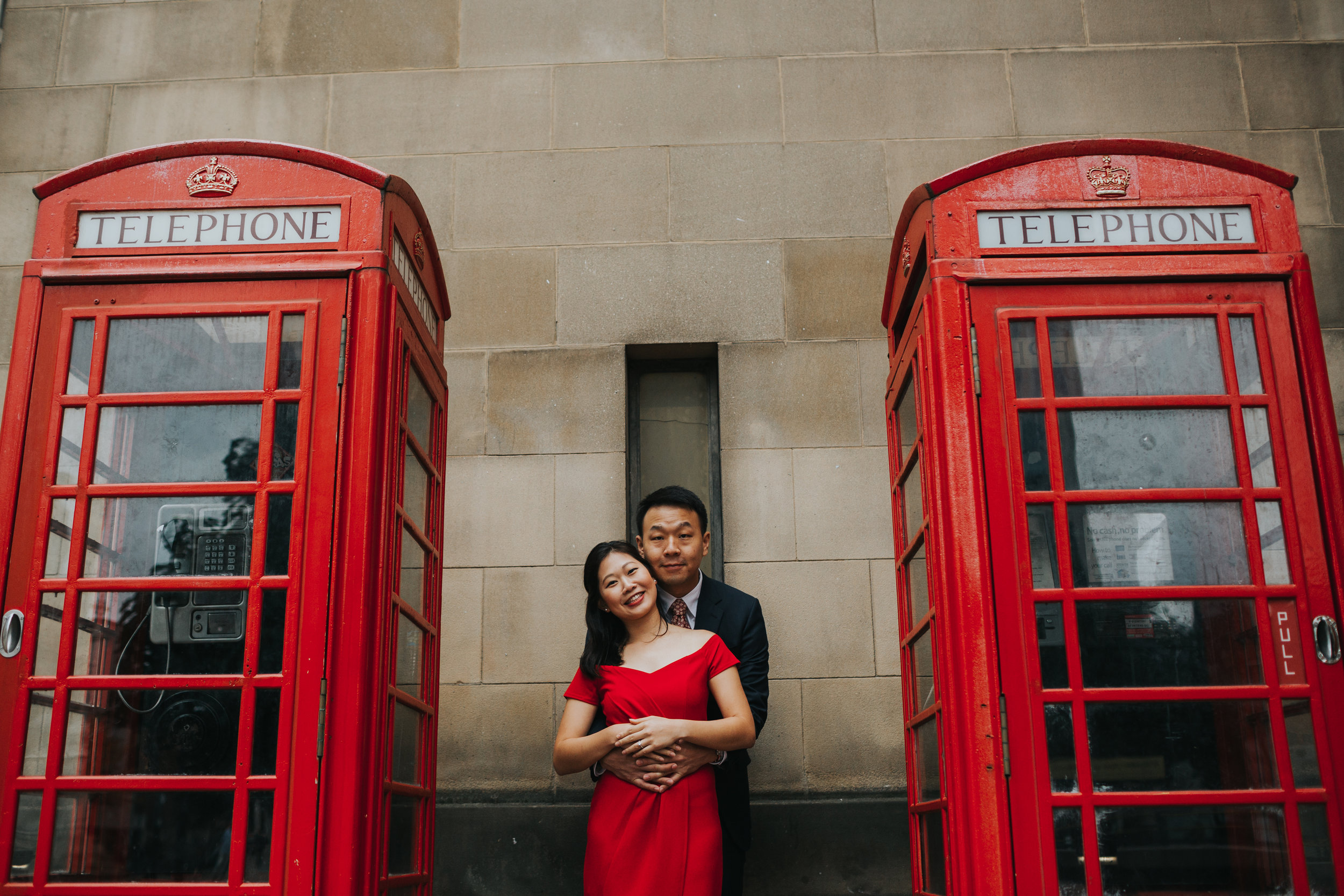 Couple cuddle in between two red phone boxes Manchester.