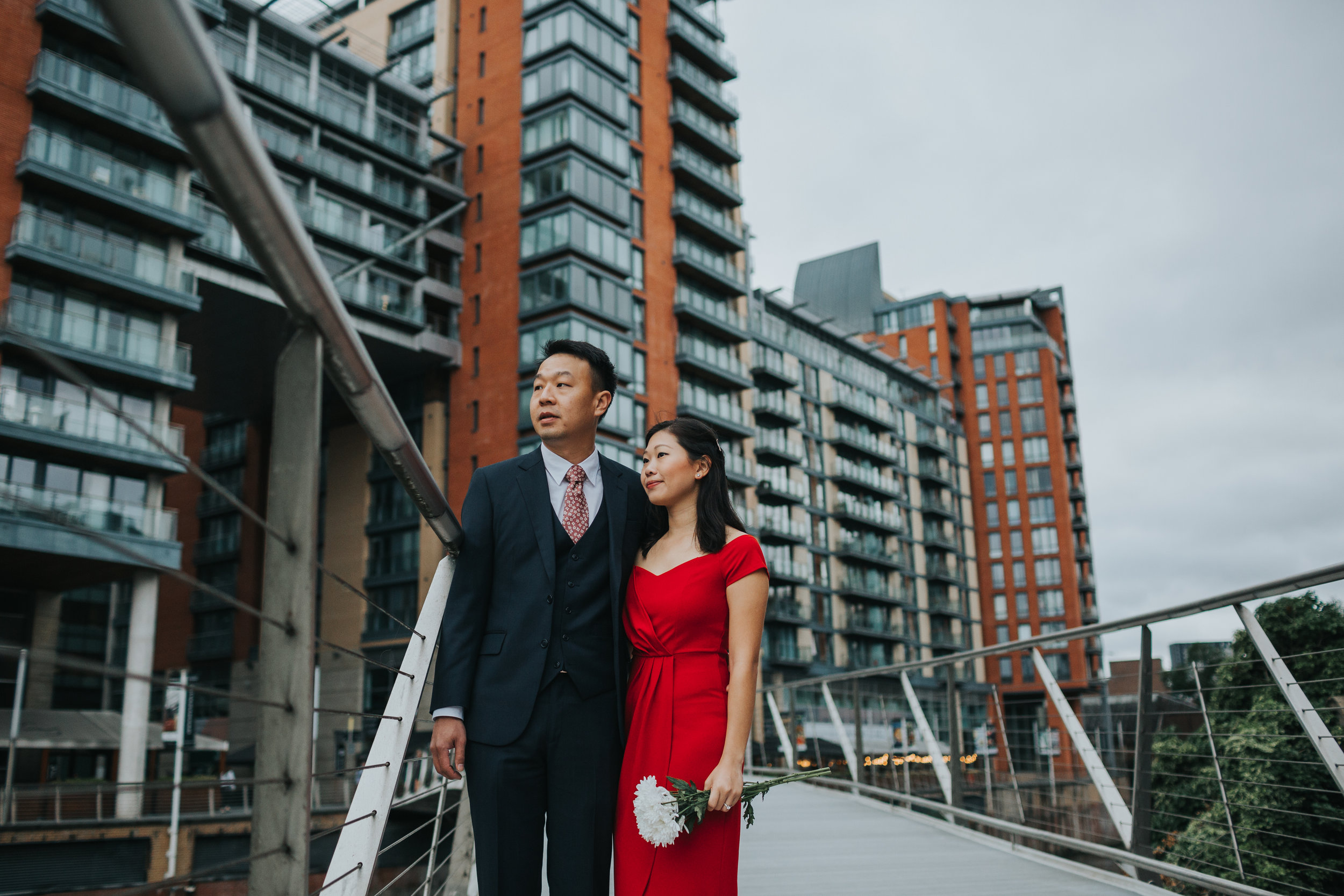 Couple stand outside Max's old University Halls on a bridge looking off into the distance. 