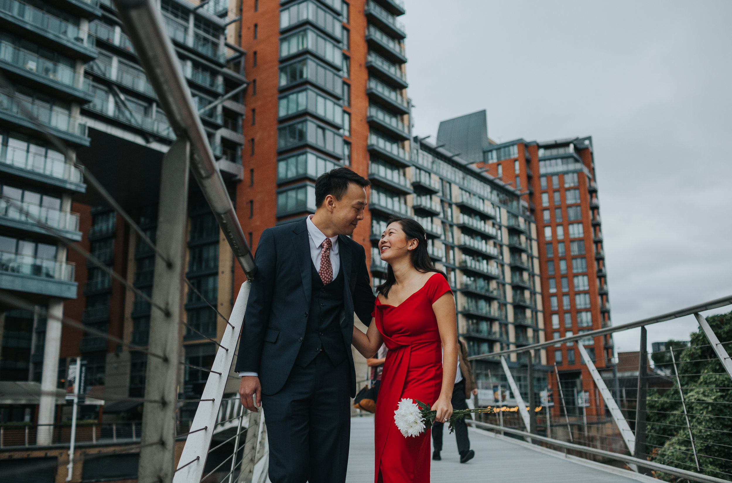 Couple stand on bridge in Manchester laughing together. 