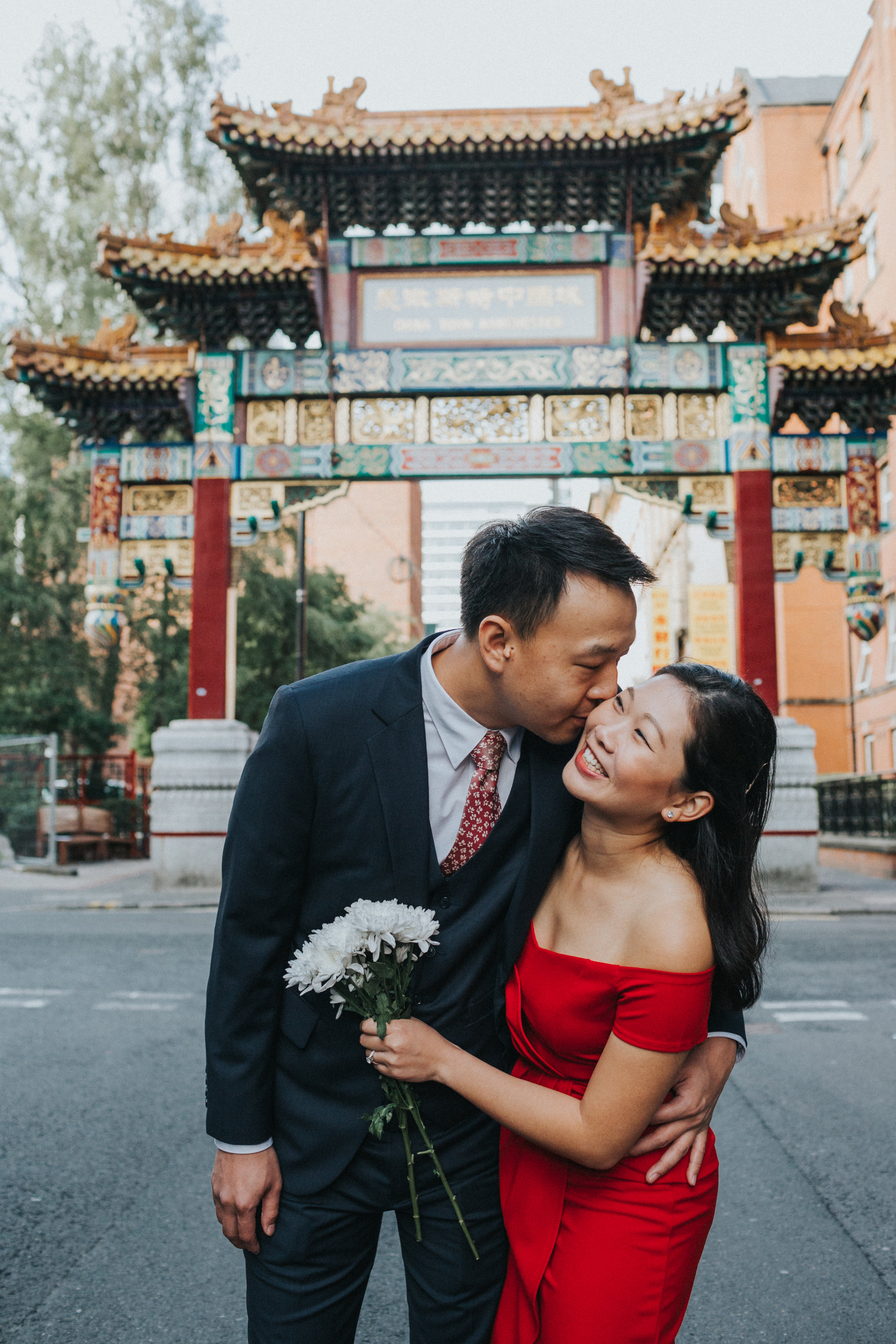 Groom gives his bride a kiss and she beams with delight under China Town Arch.