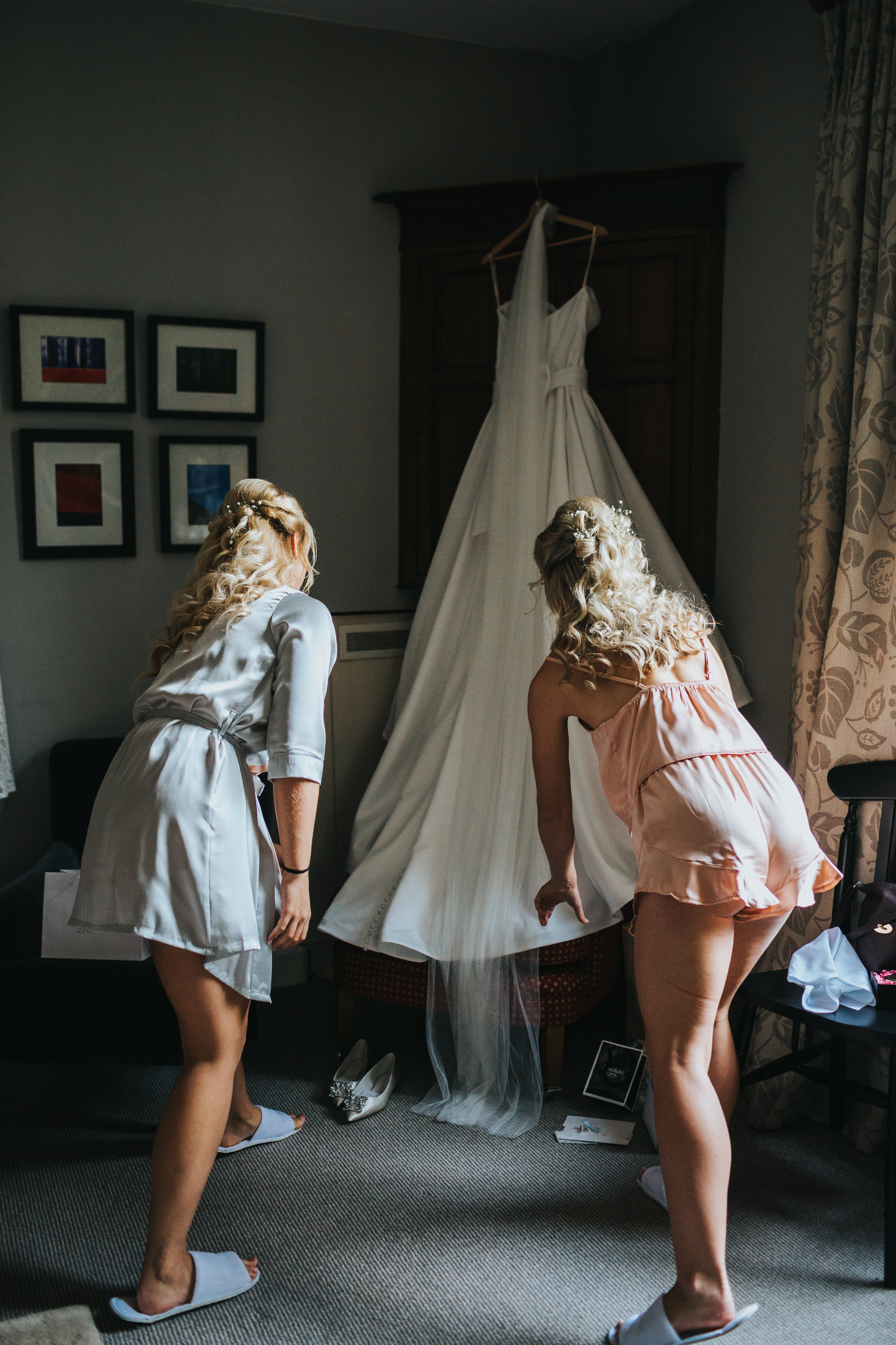 Bridesmaid help to arrange wedding dress hanging from wardrobe.