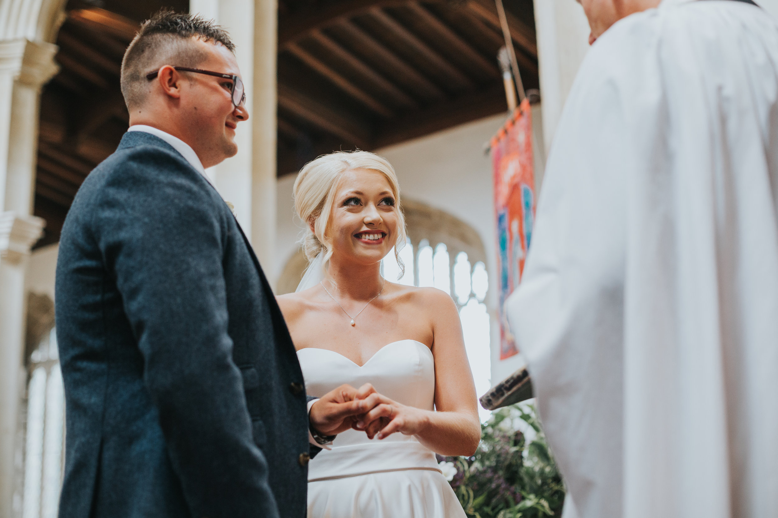 Bride and groom stand before vicar smiling.