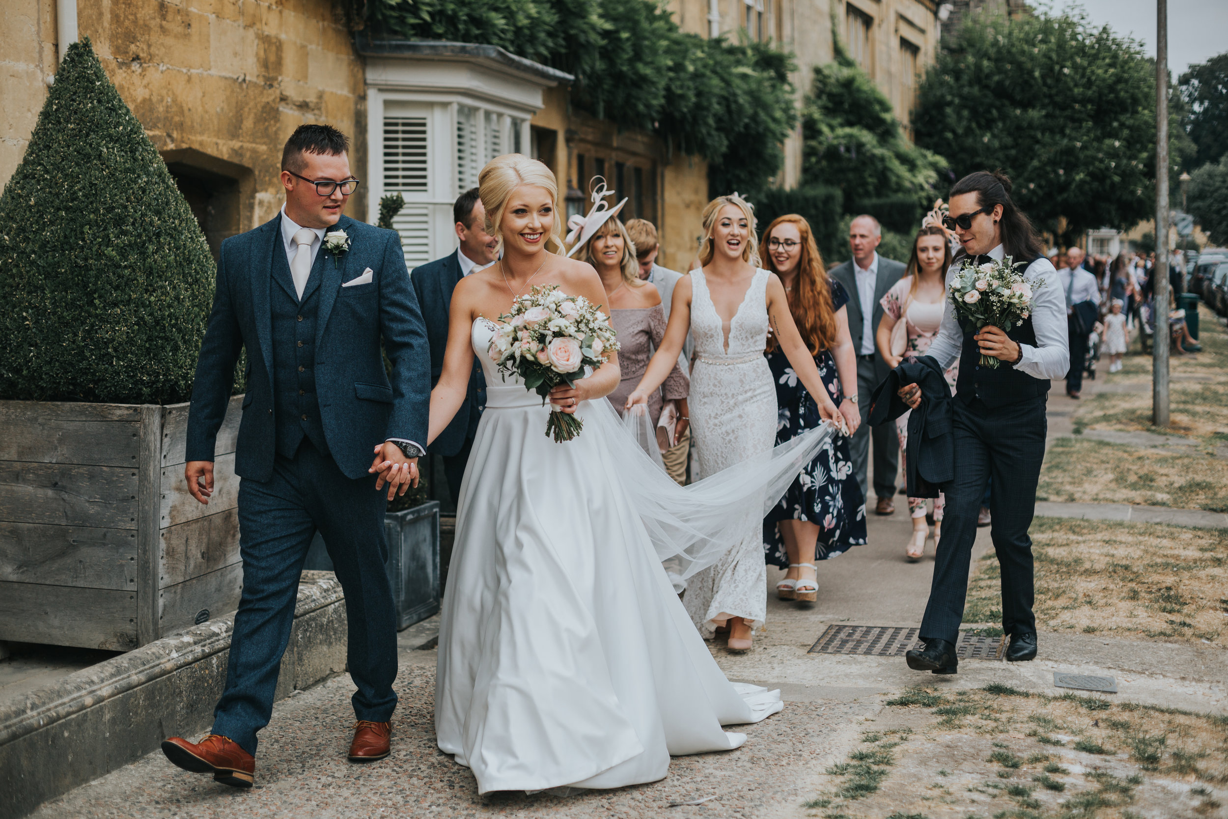 Bride and Groom leads their wedding guests down the street.  (Copy)