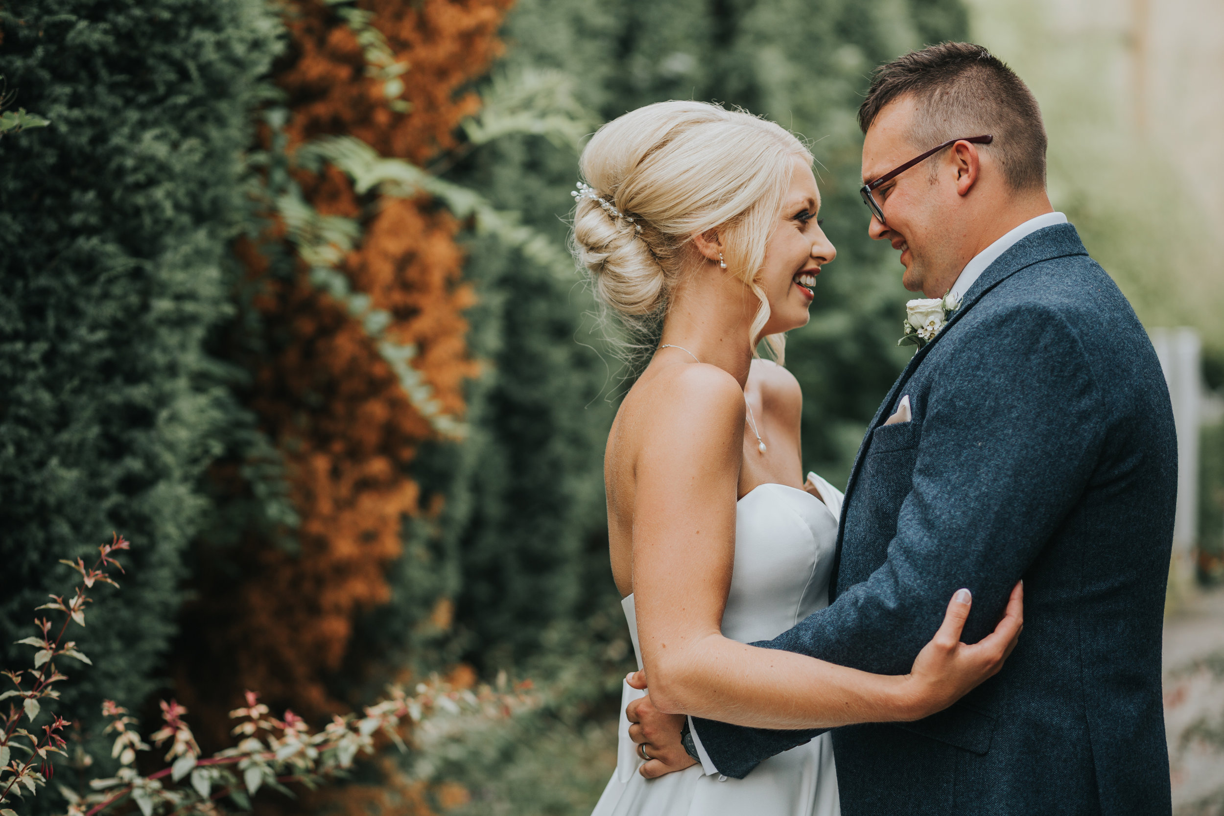 Bride and Groom Holding on and other in front of a row of tall trees.