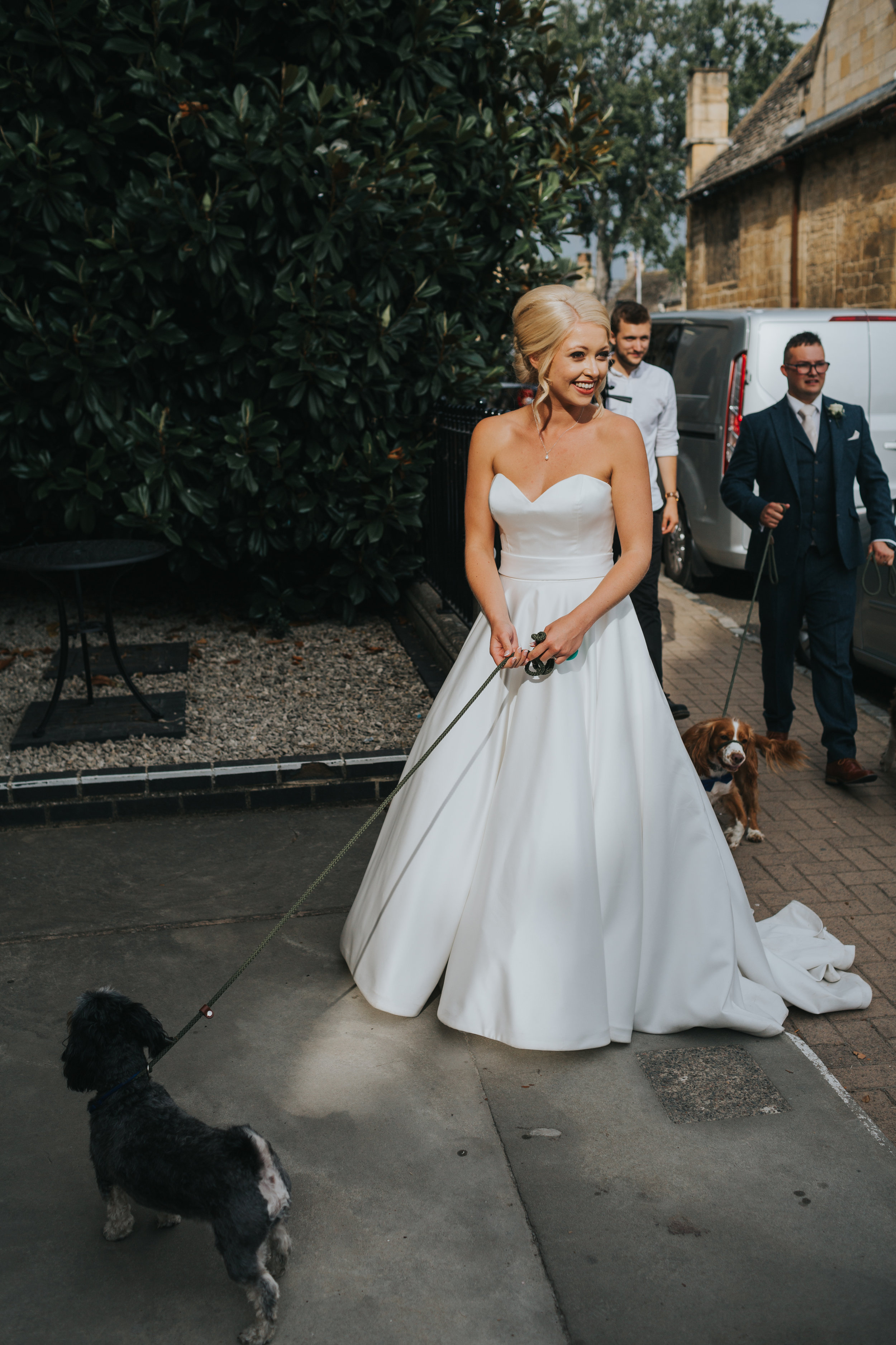 Bride stands in the sunlight holding her dog on a lead. (Copy)