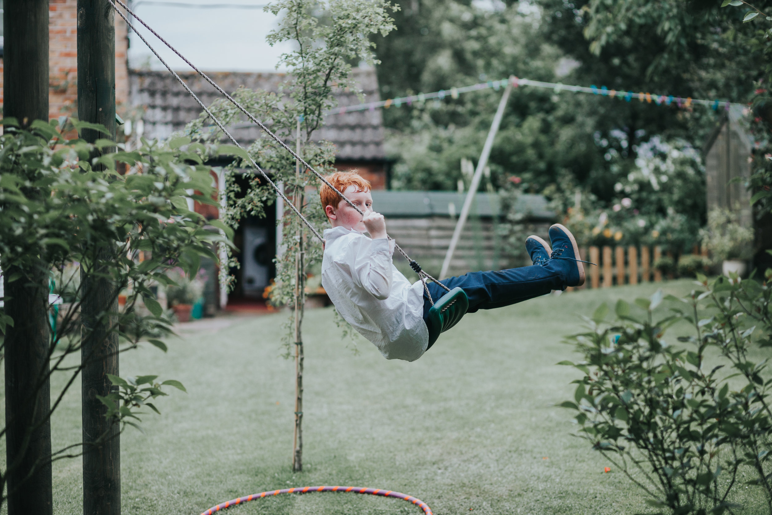 Red haired child catches photographer taking a photo of him at garden party wedding in Manchester.