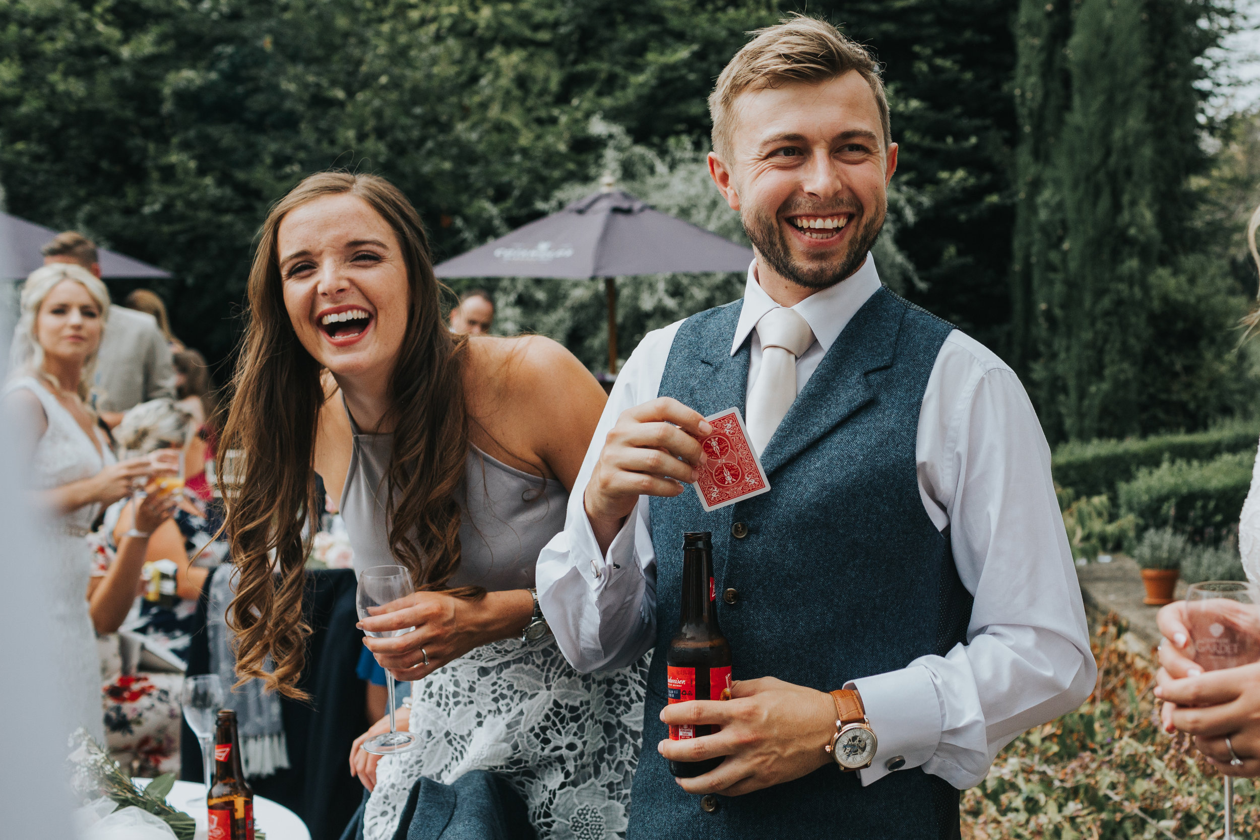 Wedding guests laugh together while playing cards at outdoor wedding, UK.