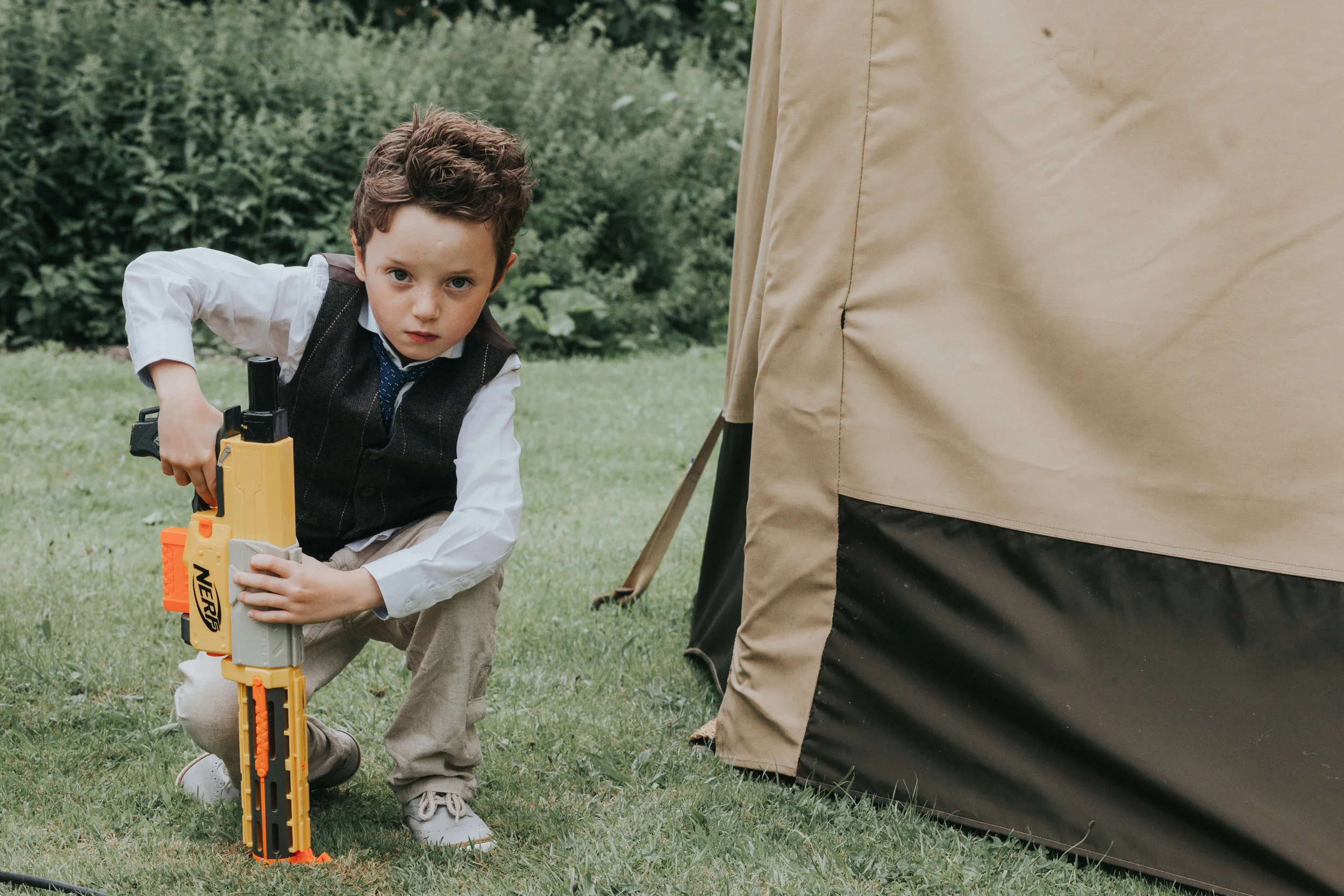 Child crouches down behind tipi, holding his water gun ready to wreak havock on unsuspecting wedding guests. 