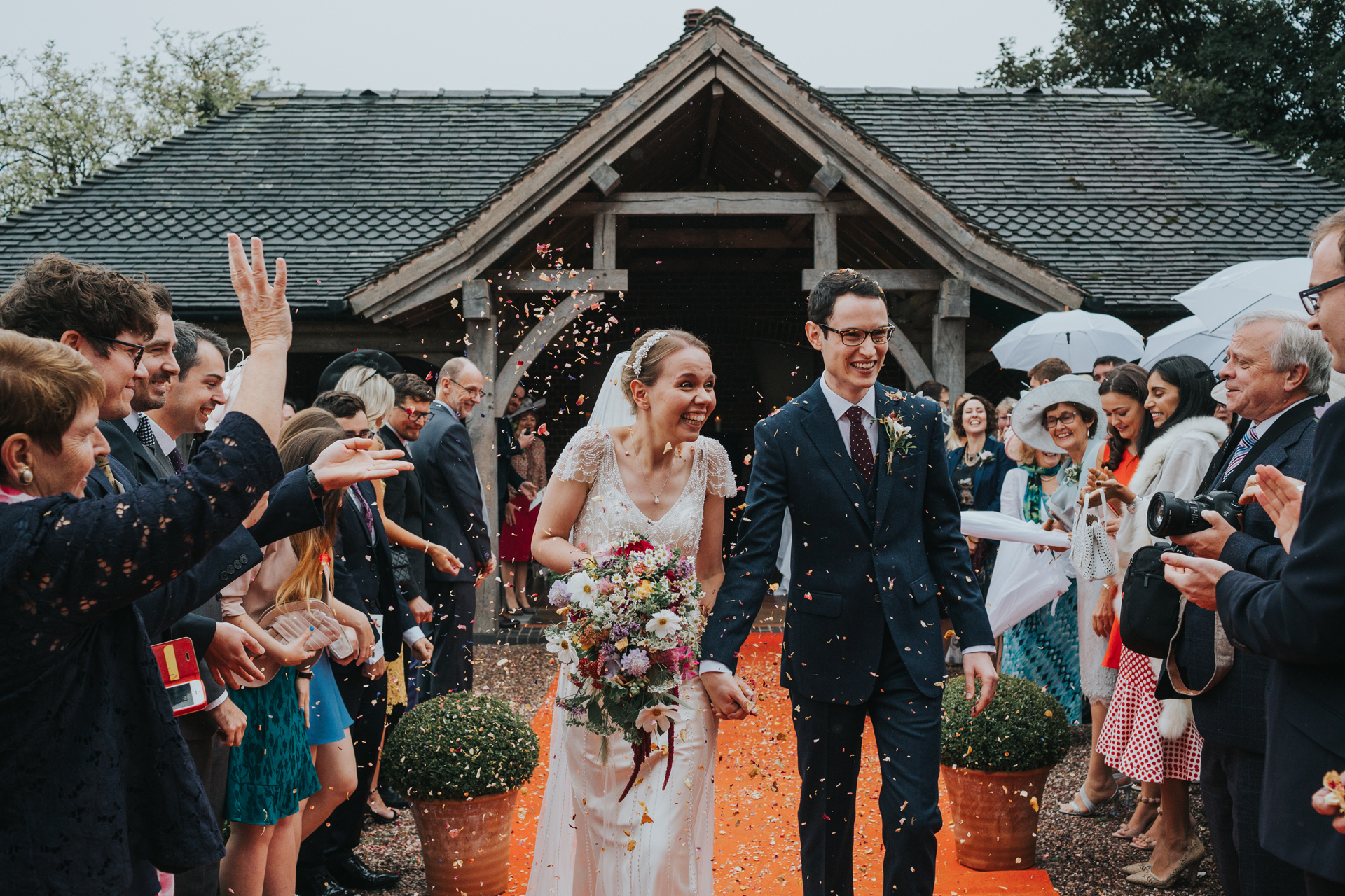 The bride and groom smile at their friends and family as they walk down the red carpet and have confetti thrown at them.