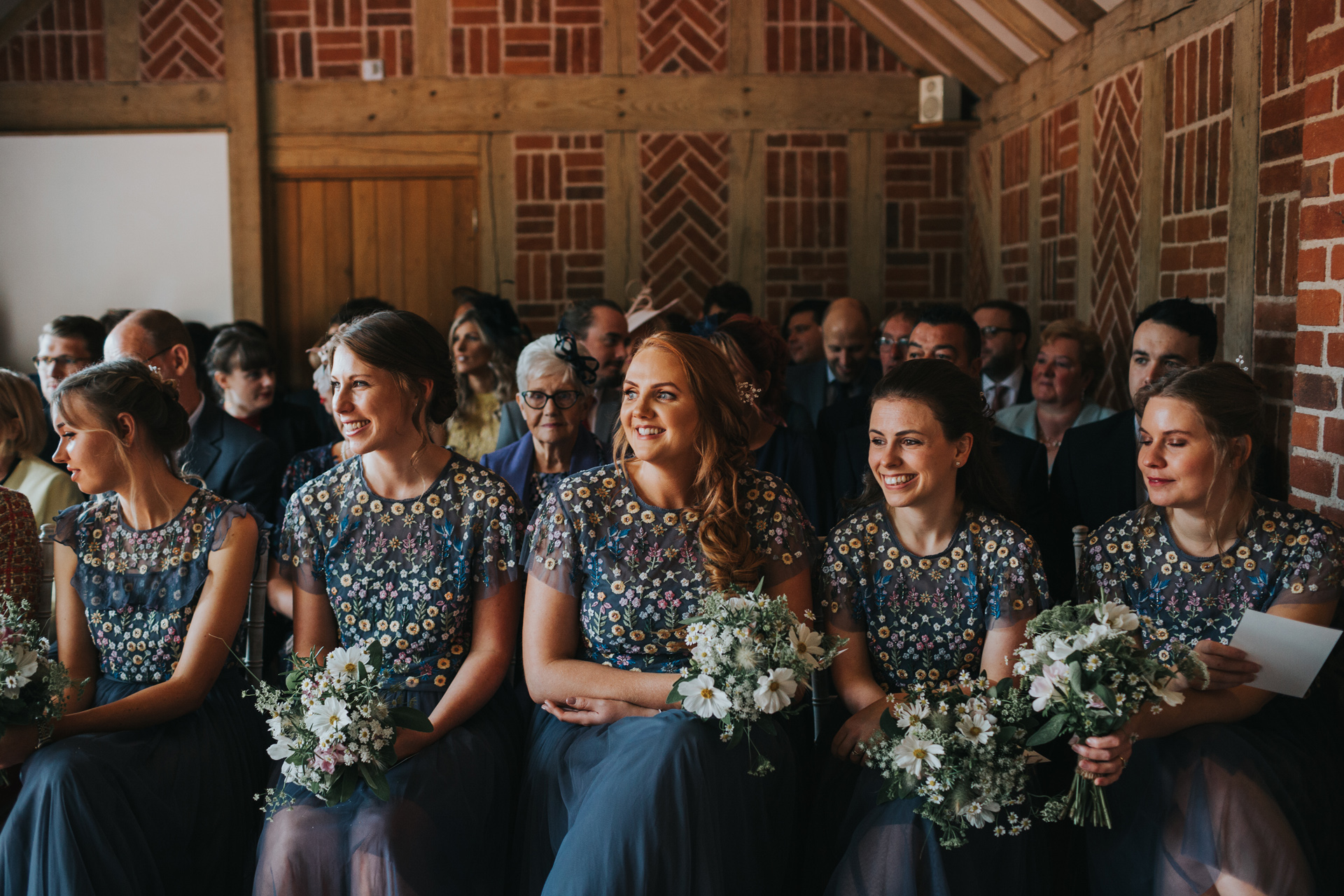 Bridesmaids sit together during the ceremony holding their bouquets. 