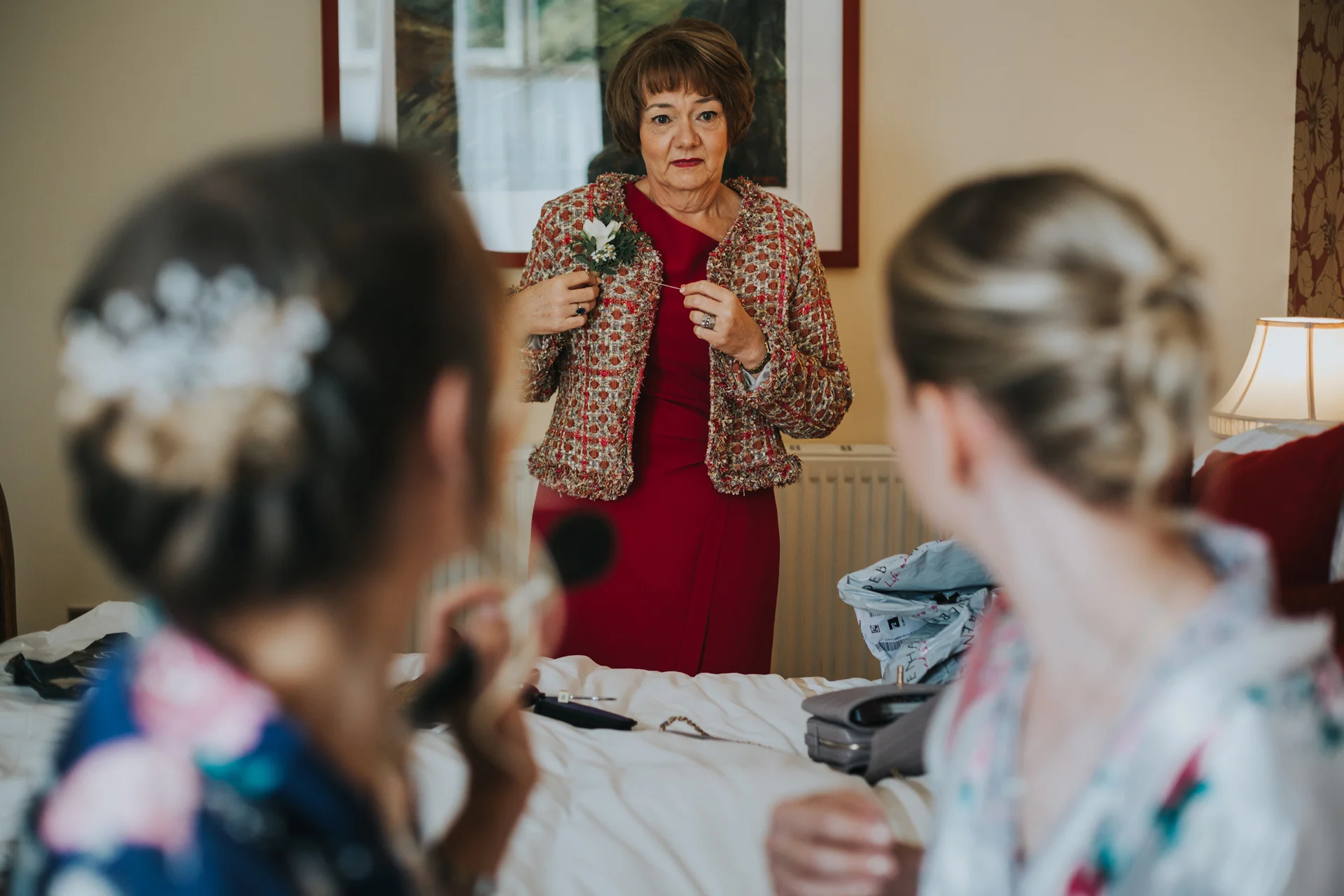 Mother of the bride puts on her corsarge while her daughters look at her. 