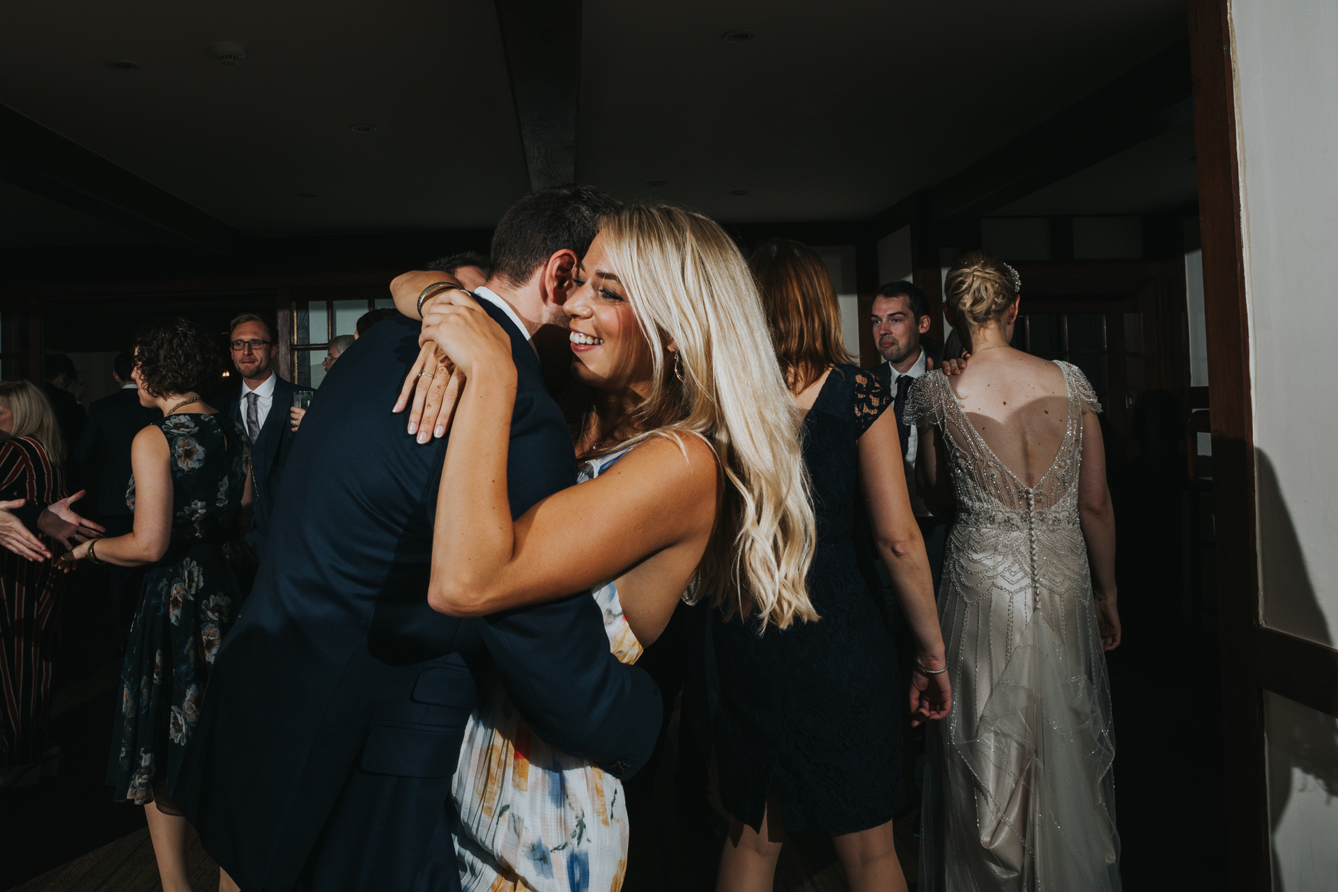 Blonde female wedding guest hugs another wedding guest while dancing together. 